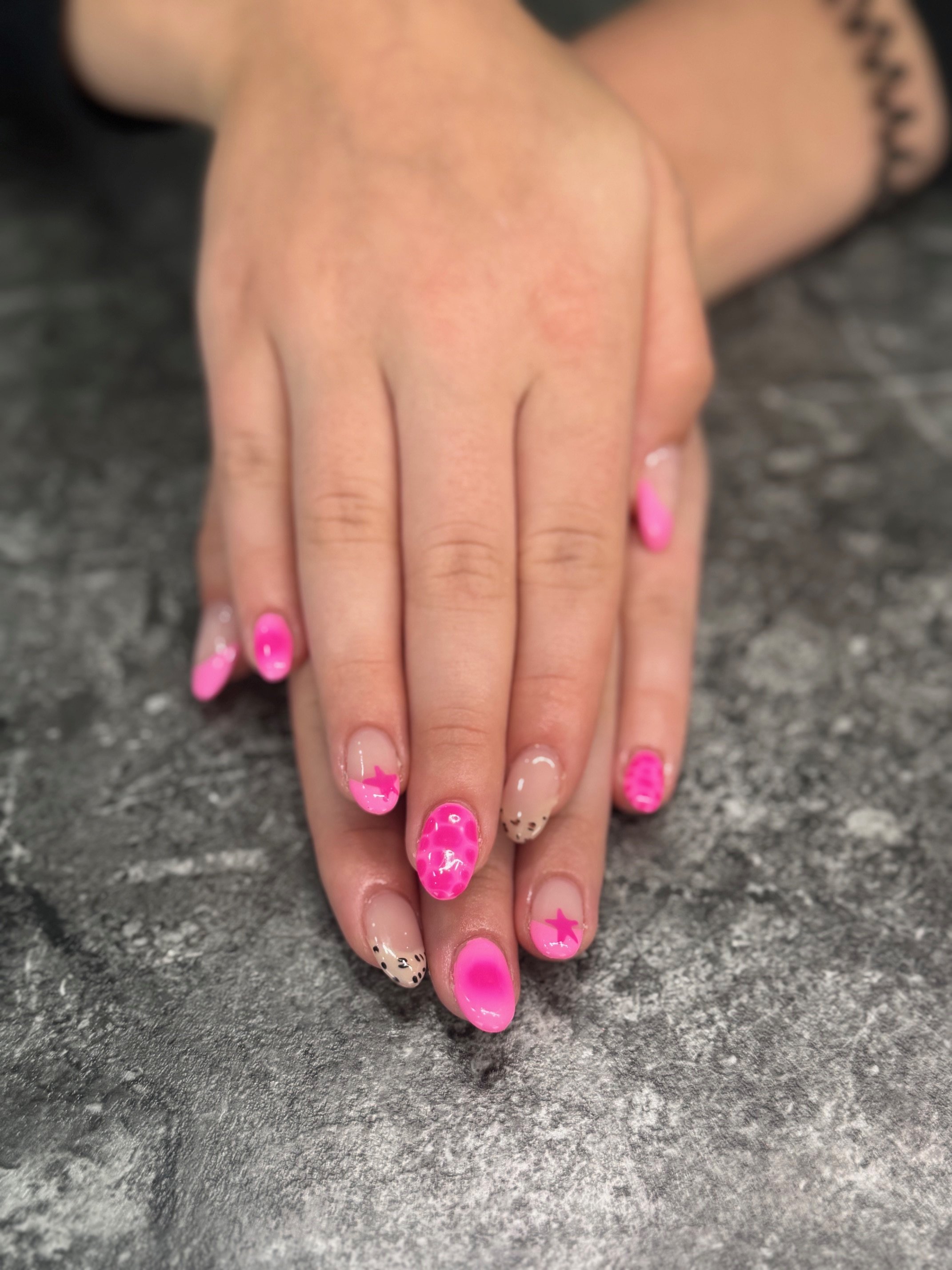 Close-up of a woman's hands with pink and beige decorated nails resting on a dark grey surface.