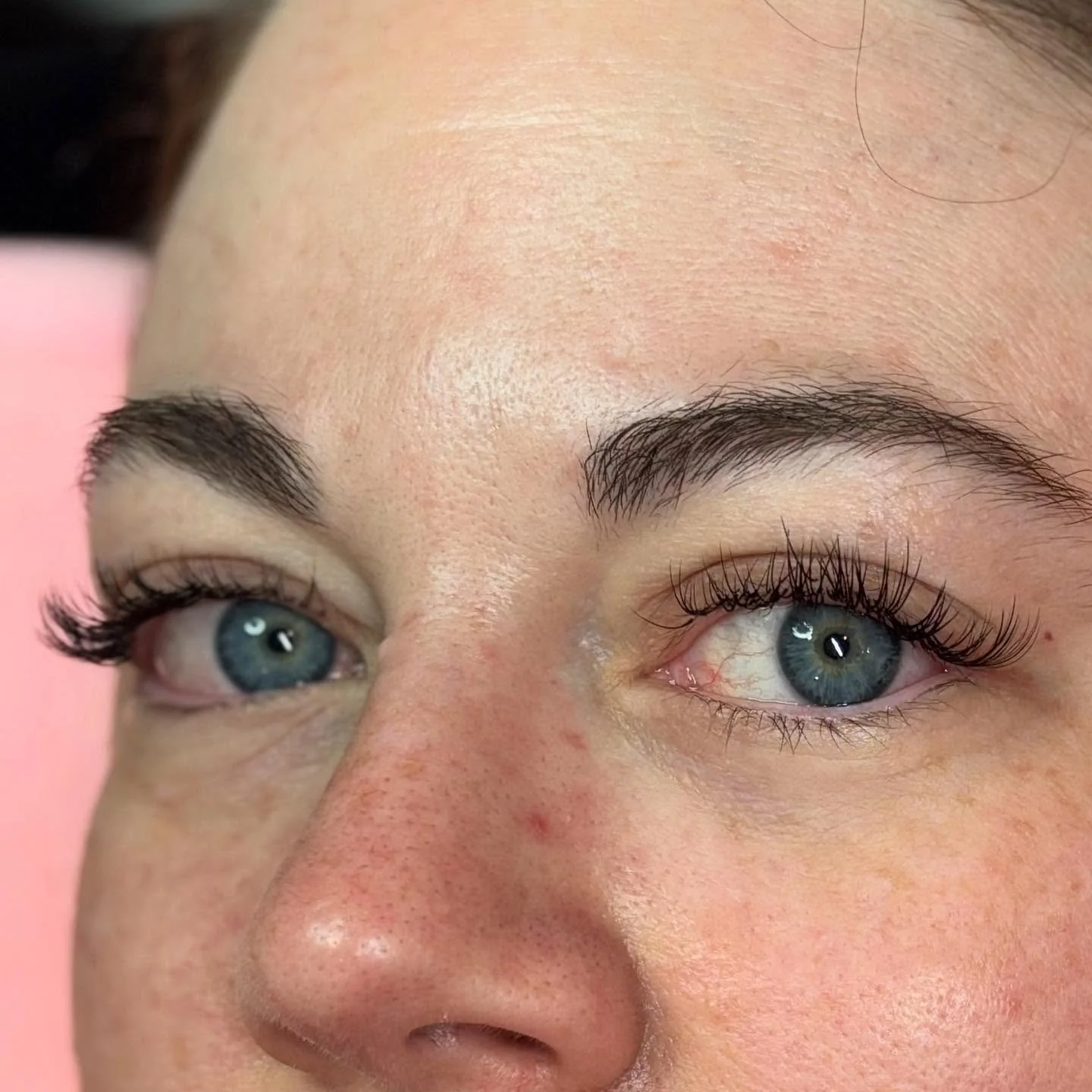 Close-up of a woman's face, focusing on her blue eyes, with applied eyelash extensions, well-groomed eyebrows, and a smooth complexion.