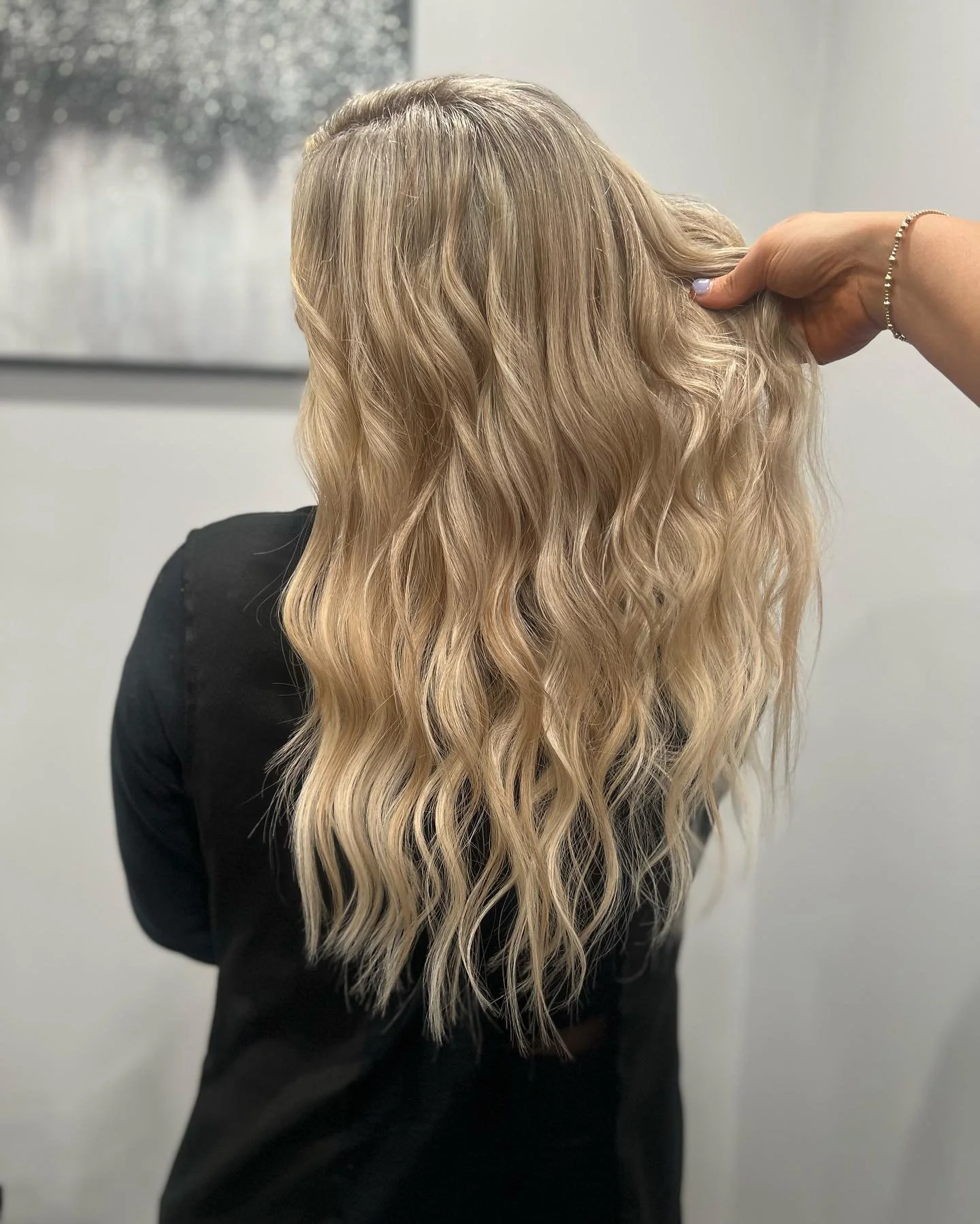 Person with long, wavy blonde hair seen from behind, with a hand holding part of the hair.