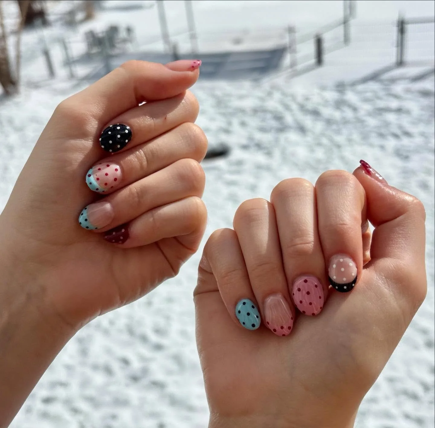 Close-up of two hands with decorated nails, against a snowy outdoor background with a fence and trees.