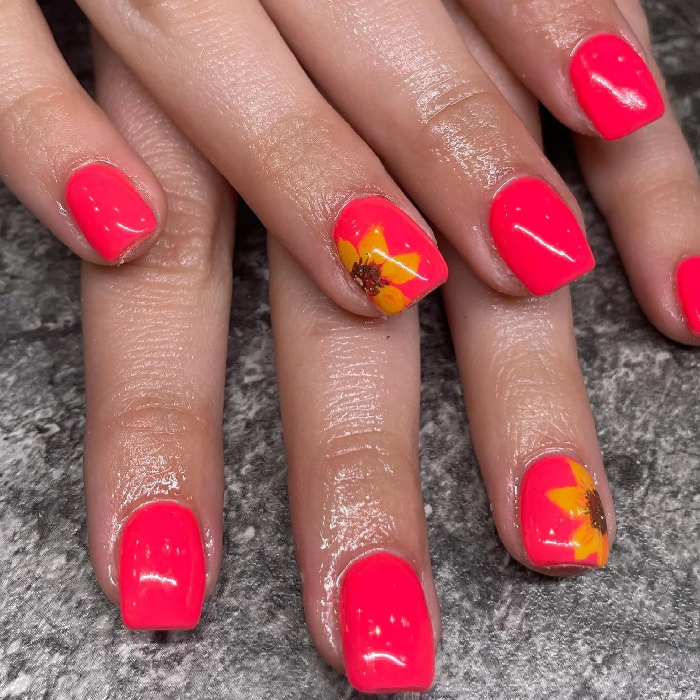 Manicured fingernails with bright pink nail polish, some nails have yellow and orange flower designs.