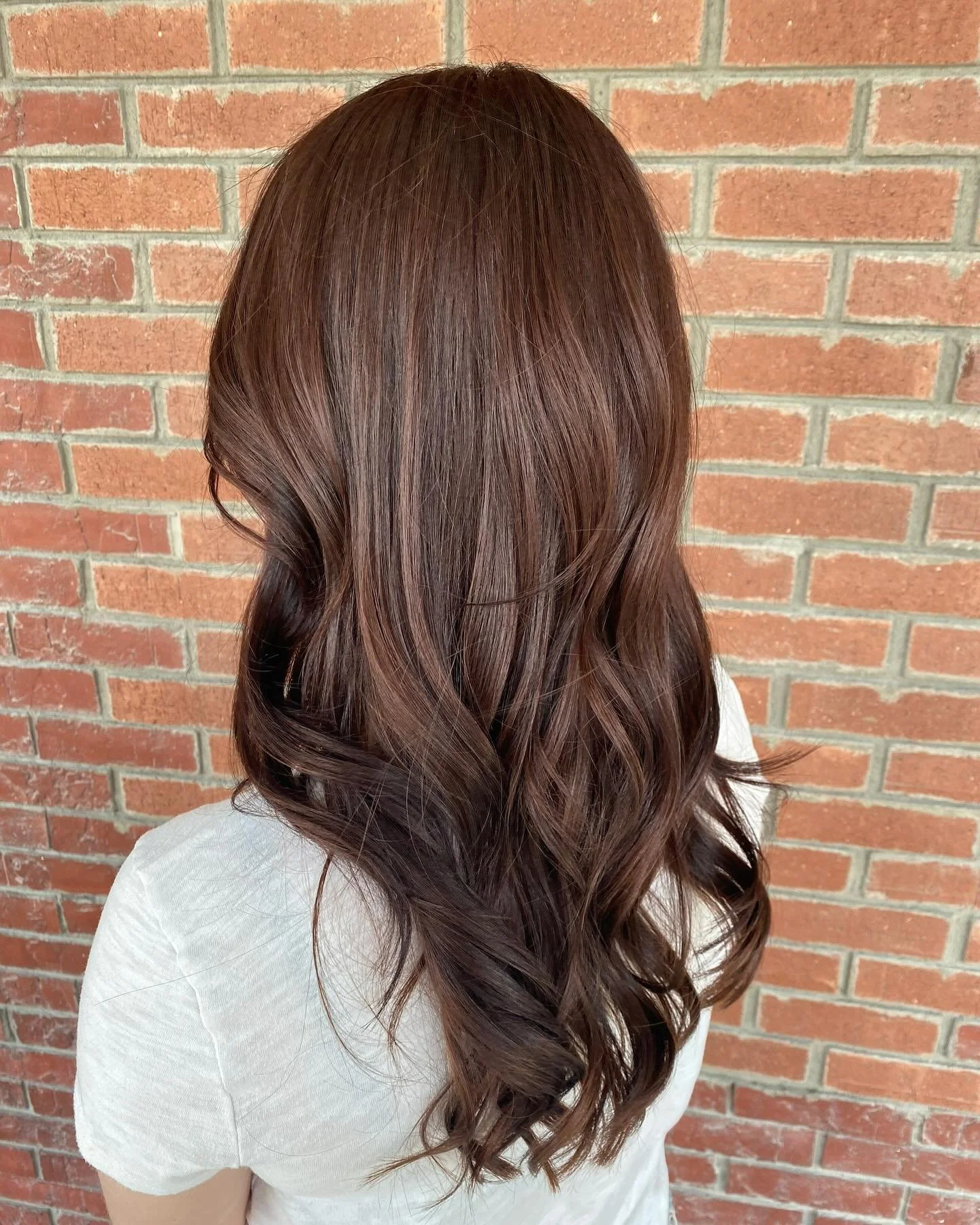 A person with long, wavy, auburn hair standing against a brick wall.