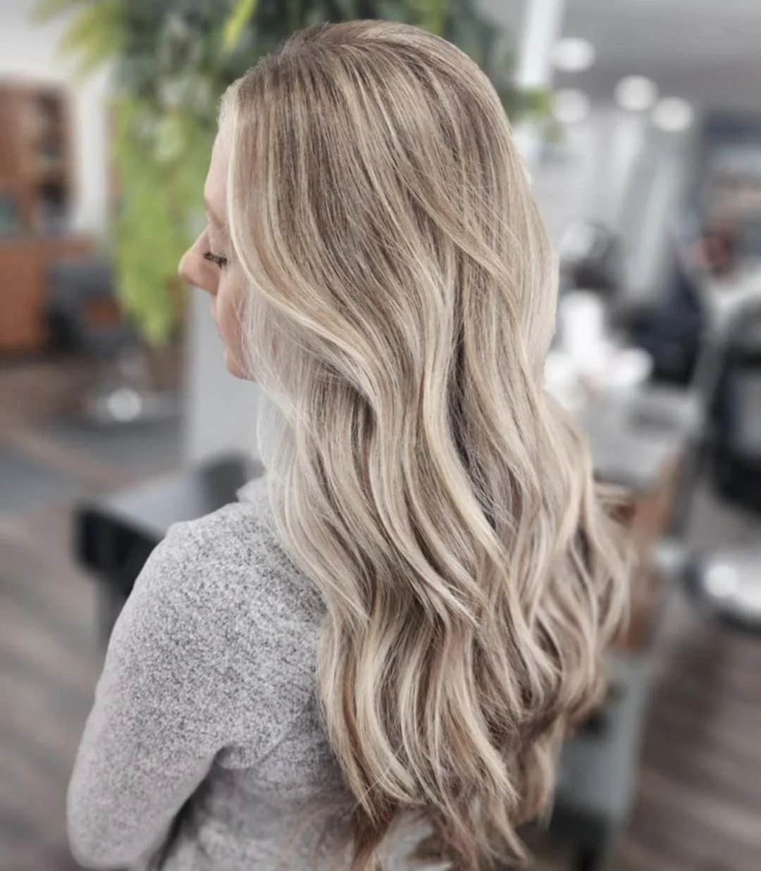 Side view of a woman with long, wavy blonde hair in a salon or home setting.