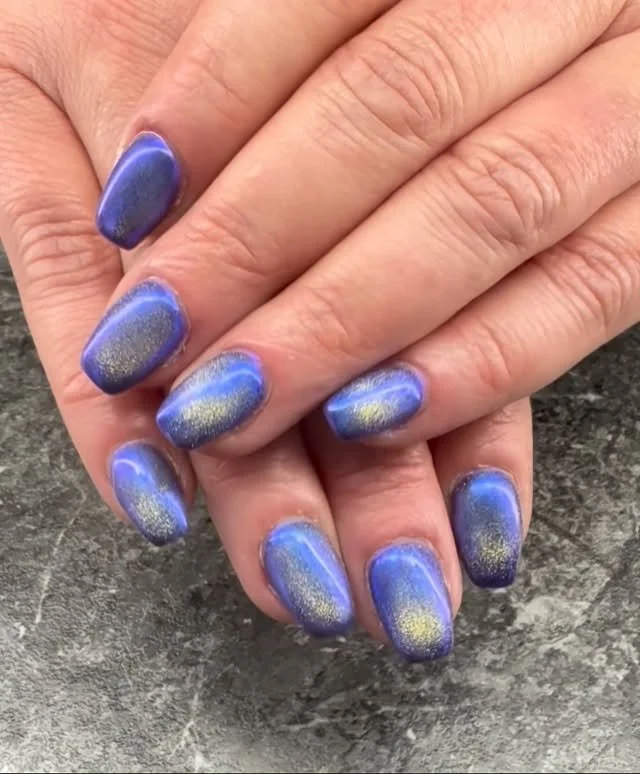 Close-up of hands with blue and gold gradient nail polish on fingernails.
