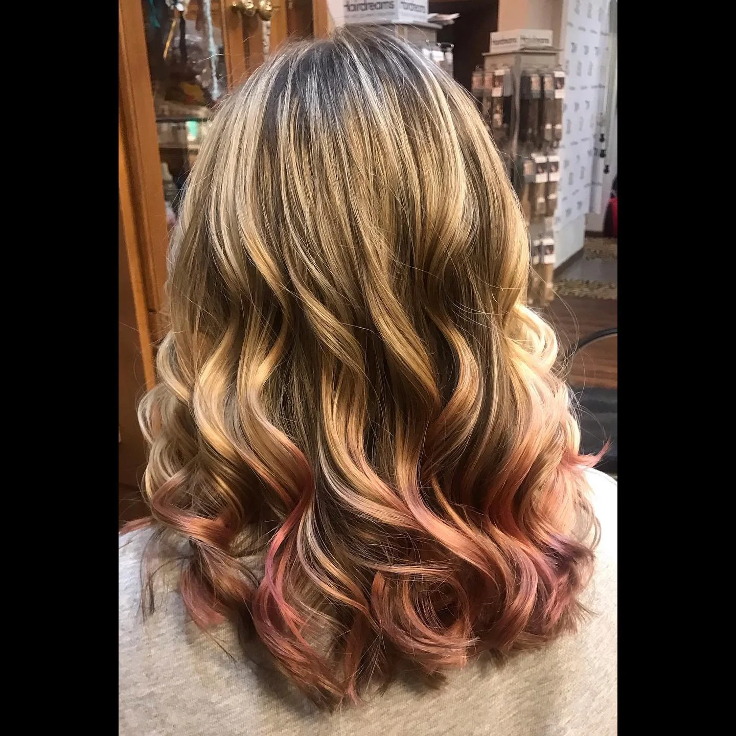 Back of a person with long, wavy hair that is blonde at the top and transitions into pink at the tips, sitting in a salon.