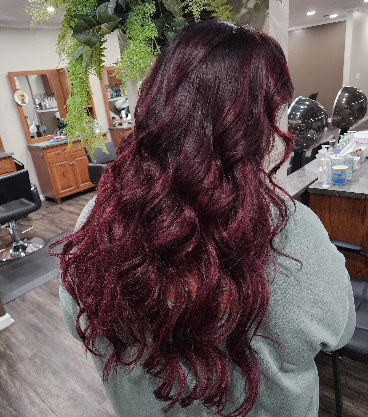 Back view of a woman with long, wavy burgundy hair in a salon setting.