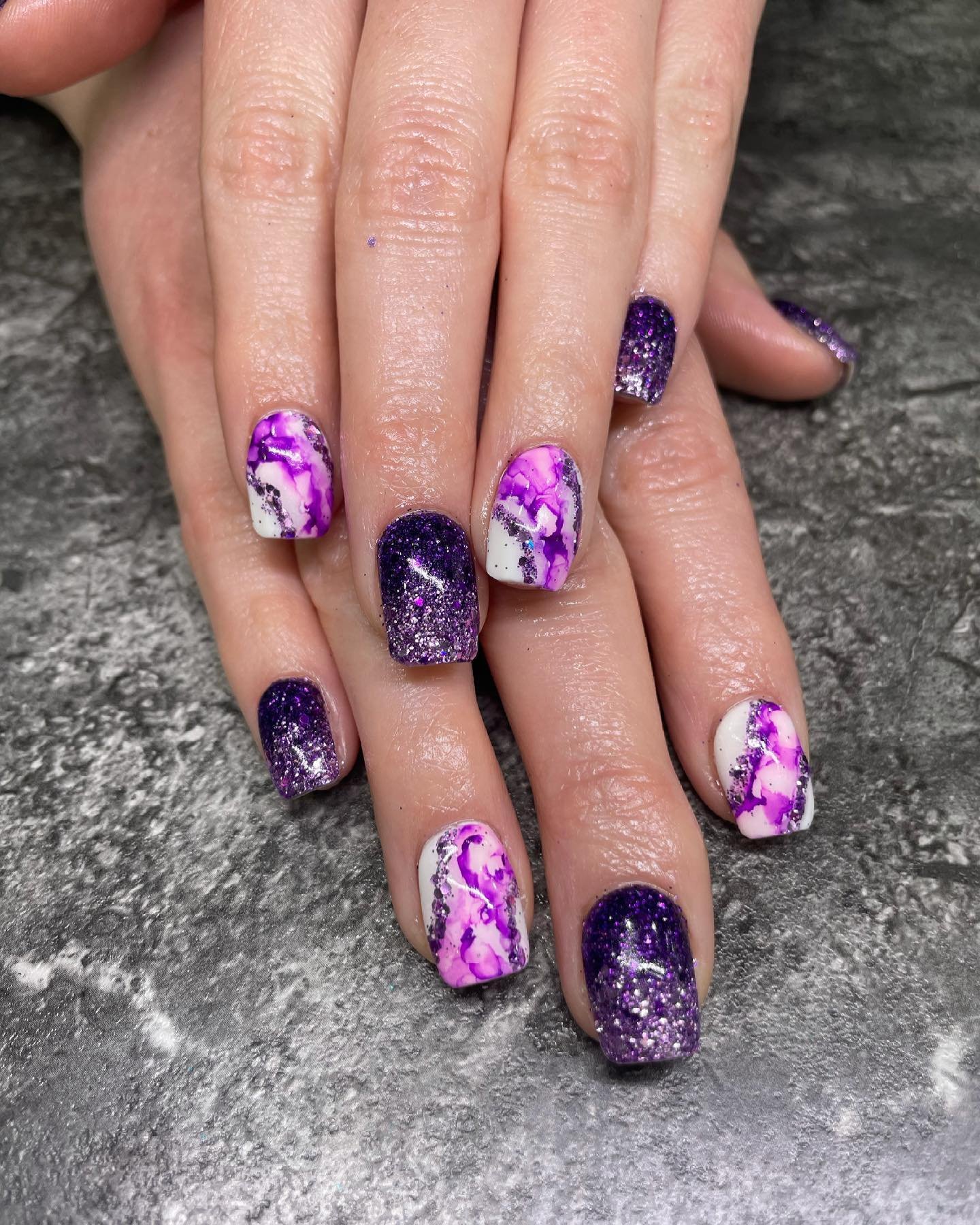 Nails with purple, pink, and white marble design and glitter accents.