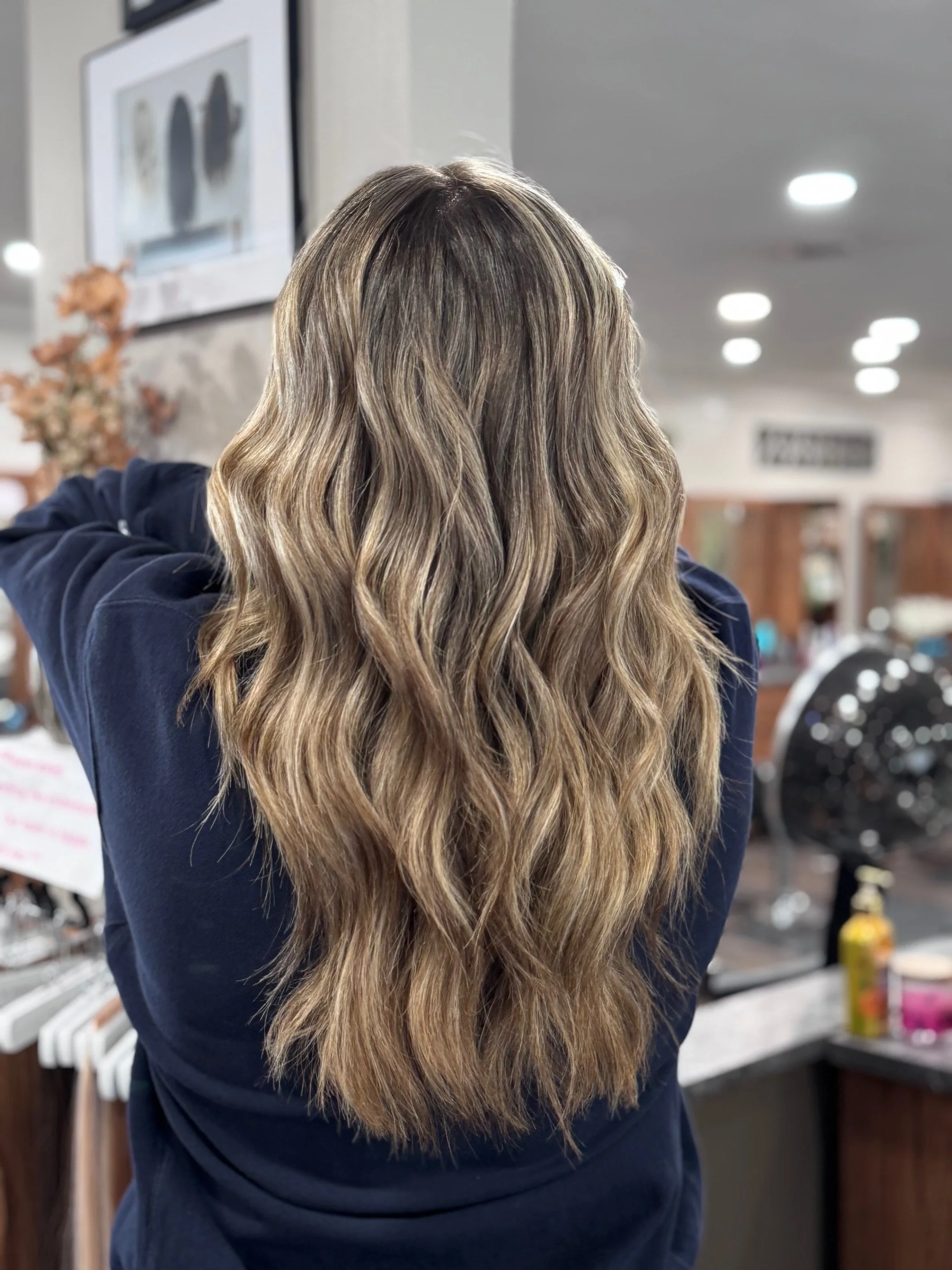 Woman with long, wavy, blonde hair standing in a salon or hair studio.