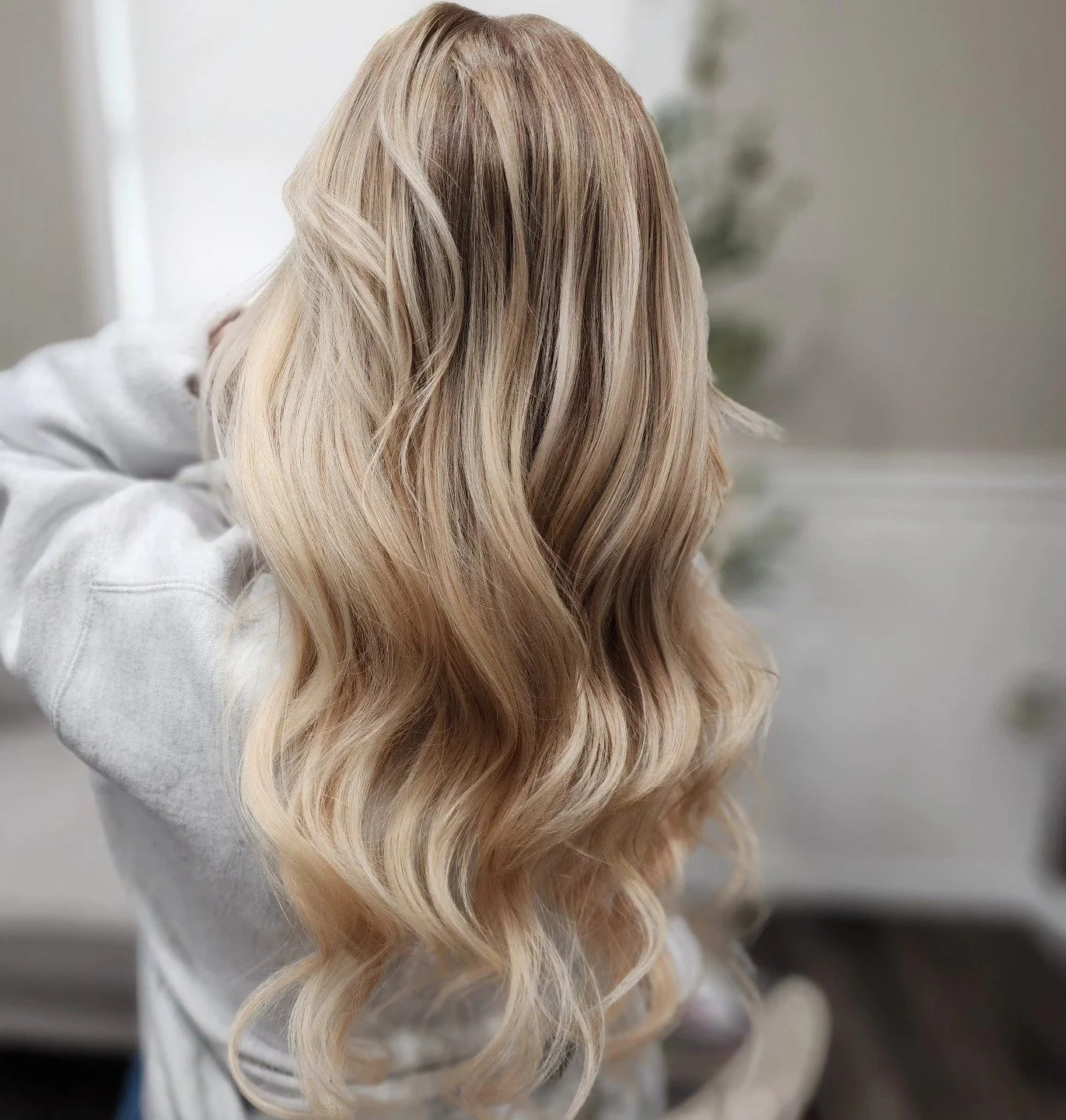 A person with long, wavy blonde hair, seen from behind, wearing a white hoodie.