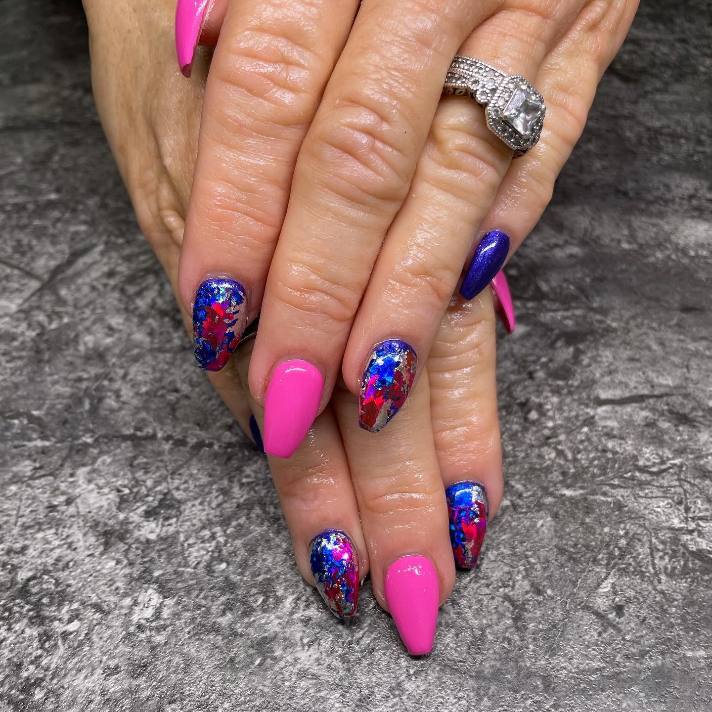 Close-up of a person's hands with colorful nail art and a silver ring with a large gemstone.