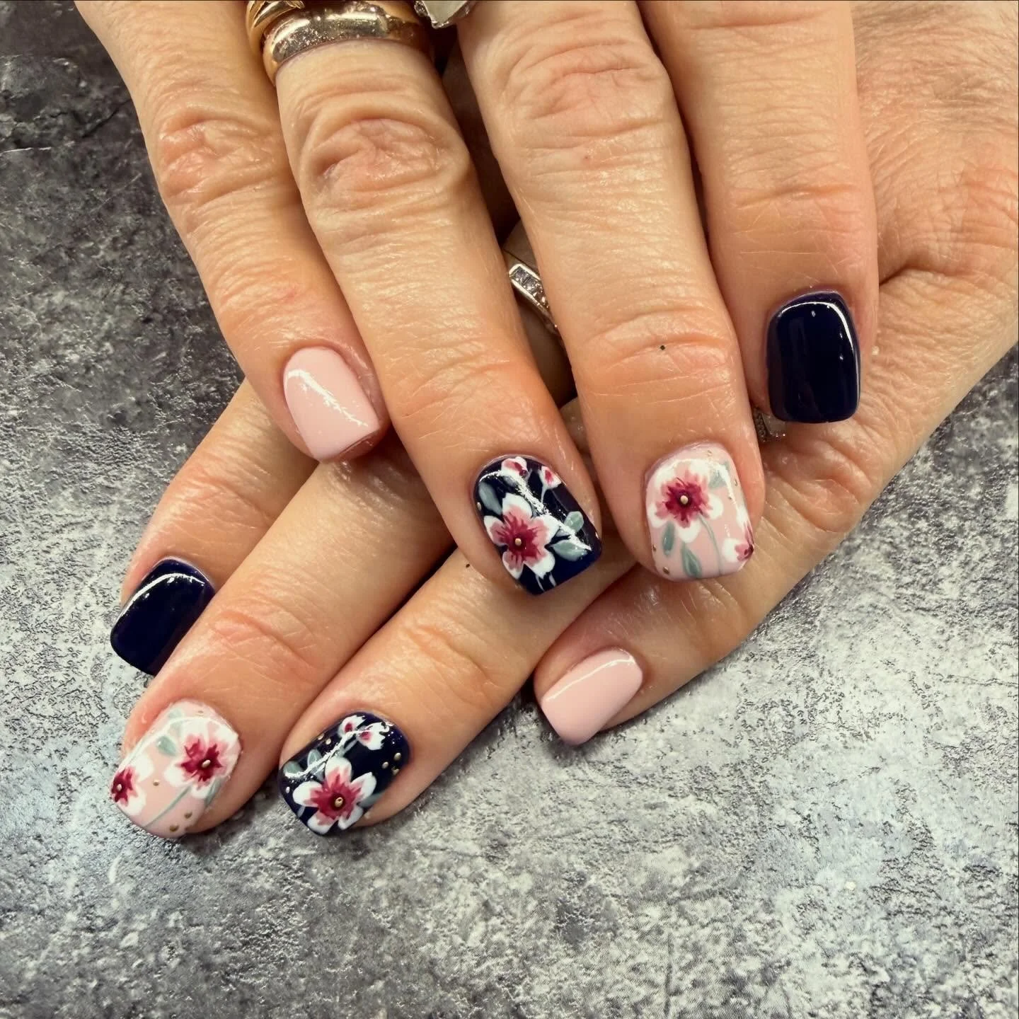 Close-up of a person's hands with floral and solid color nail polish, resting on a textured gray surface.