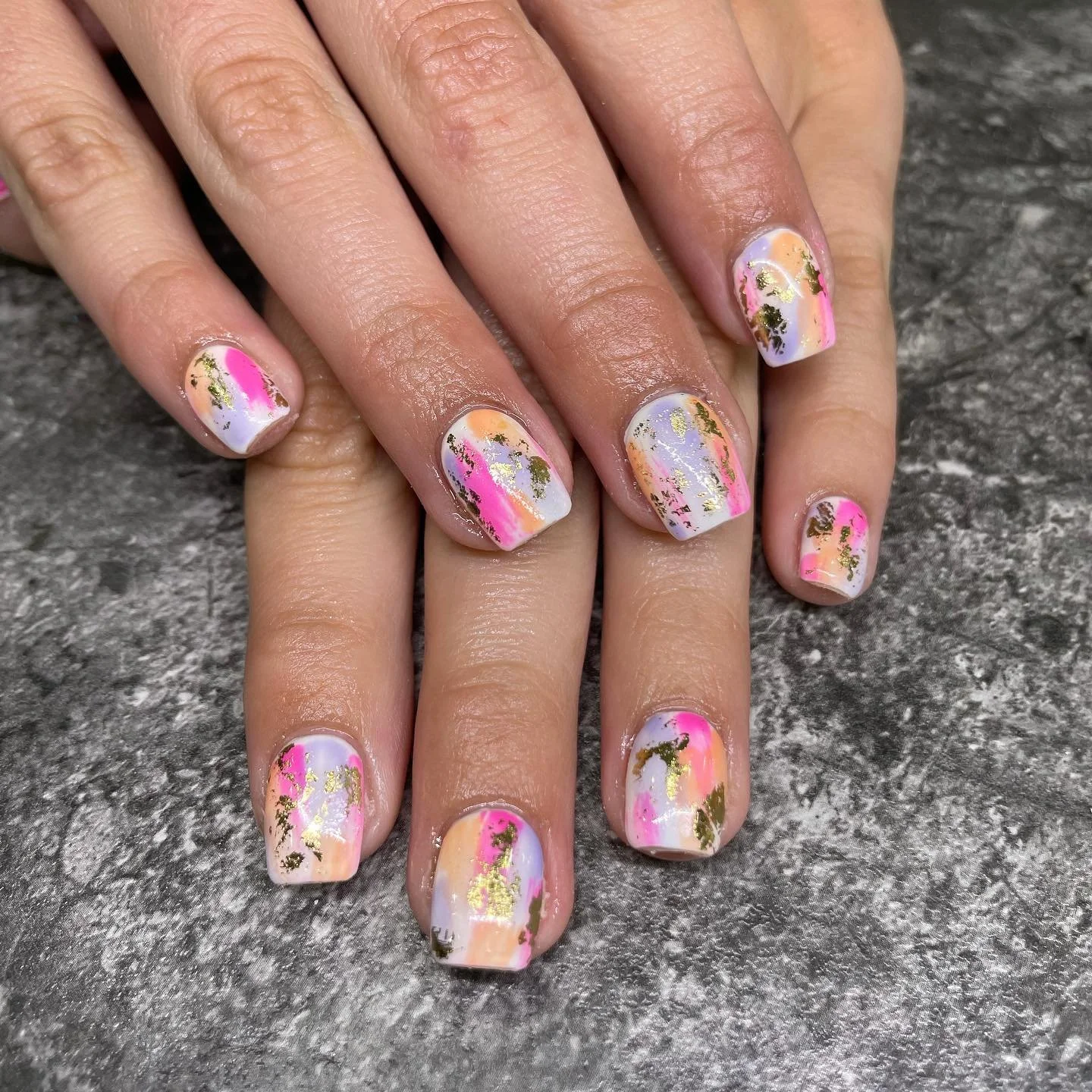 Manicured nails with colorful pastel abstract art and gold foil accents.