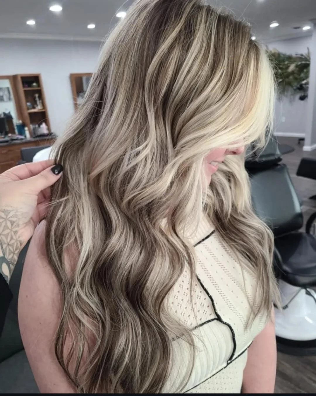 Close-up of a woman with long, wavy blonde hair, sitting in a salon or similar setting.
