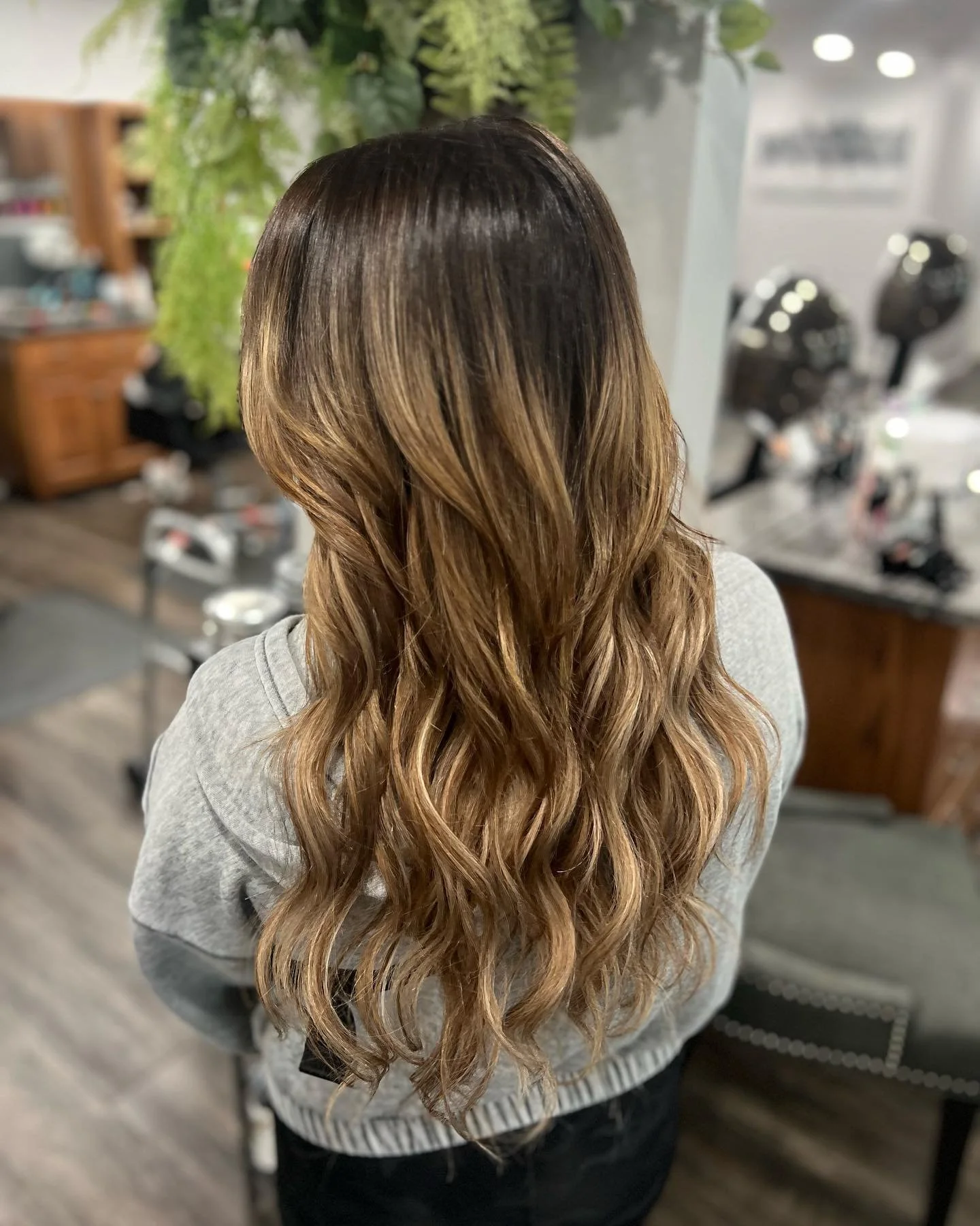 Back view of a woman with long, wavy, blonde hair in a salon setting.