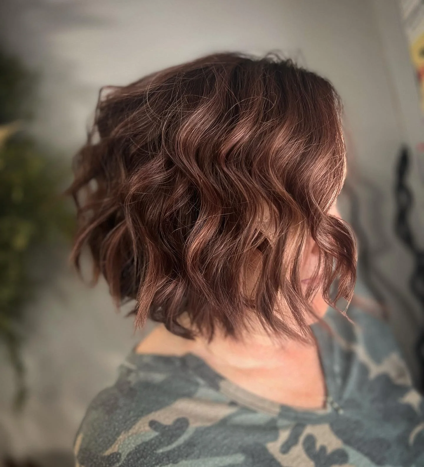 Woman with shoulder-length, wavy, brown hair, wearing a camo-patterned shirt.