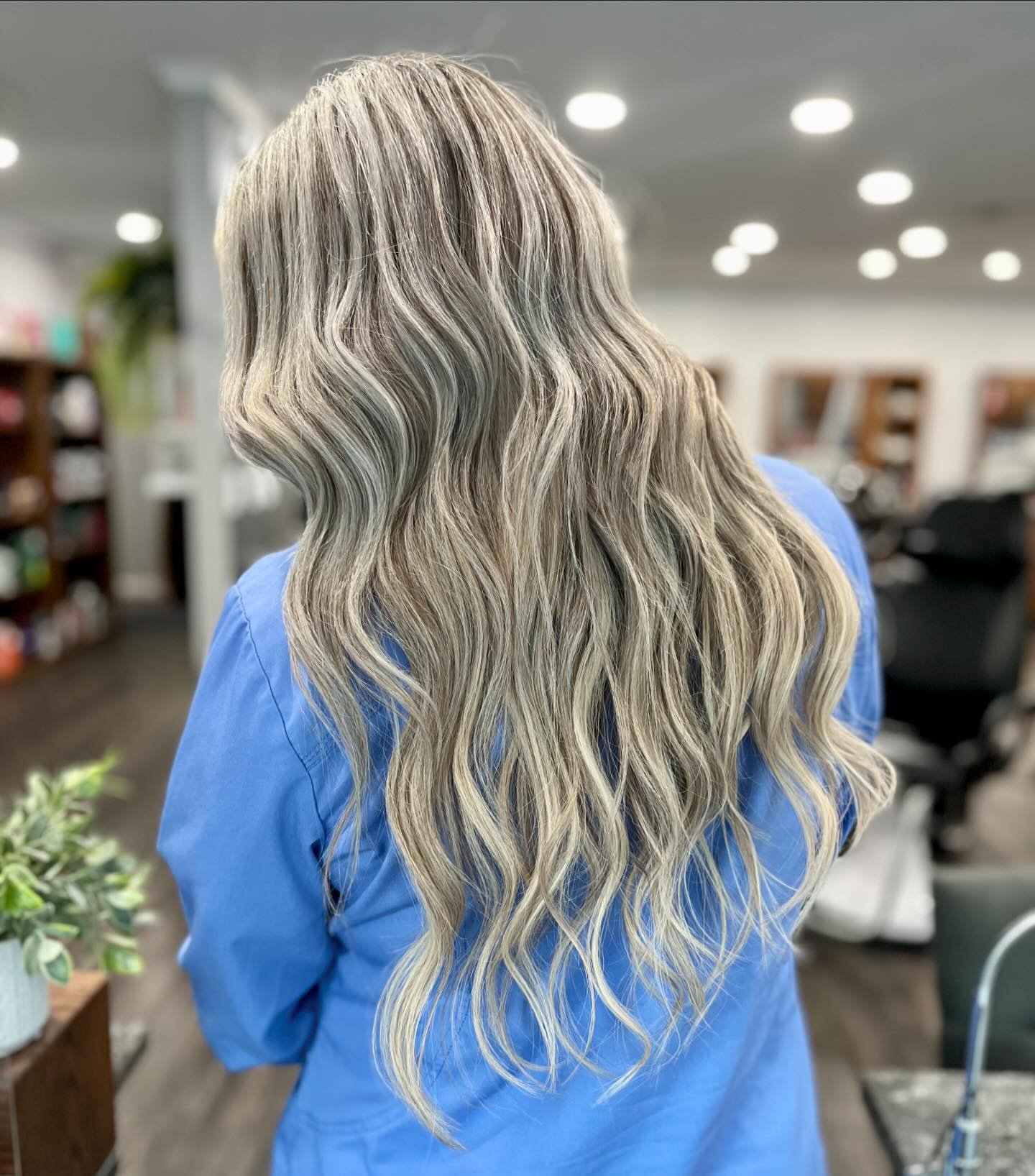 Long, wavy, blonde hair on a person wearing a blue shirt, in a salon setting.