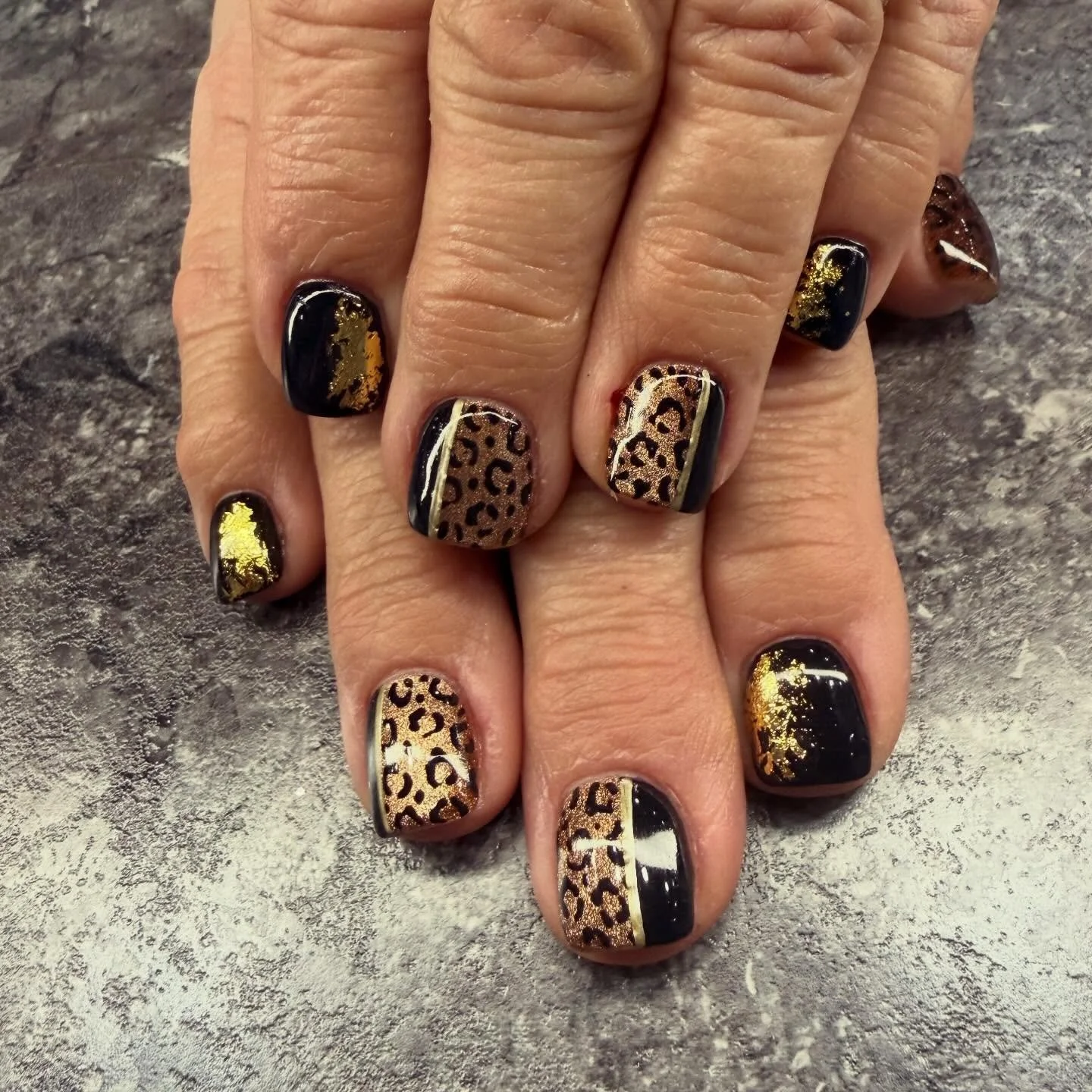 Manicure with black and gold leopard print nails and gold foil accents.