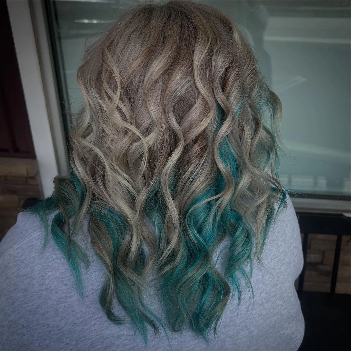 Back view of a person with shoulder-length blonde hair with turquoise tips, styled in loose waves.