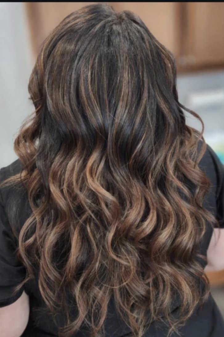 Back view of a woman with long, wavy brown hair with subtle highlights.