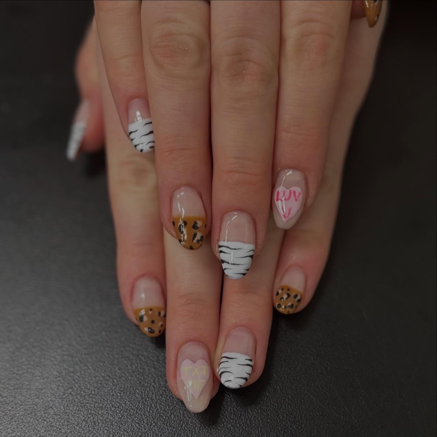 Manicured fingernails with various designs, including zebra stripes, leopard print, and words like 'LUV' and 'XOXO' on a pink heart.