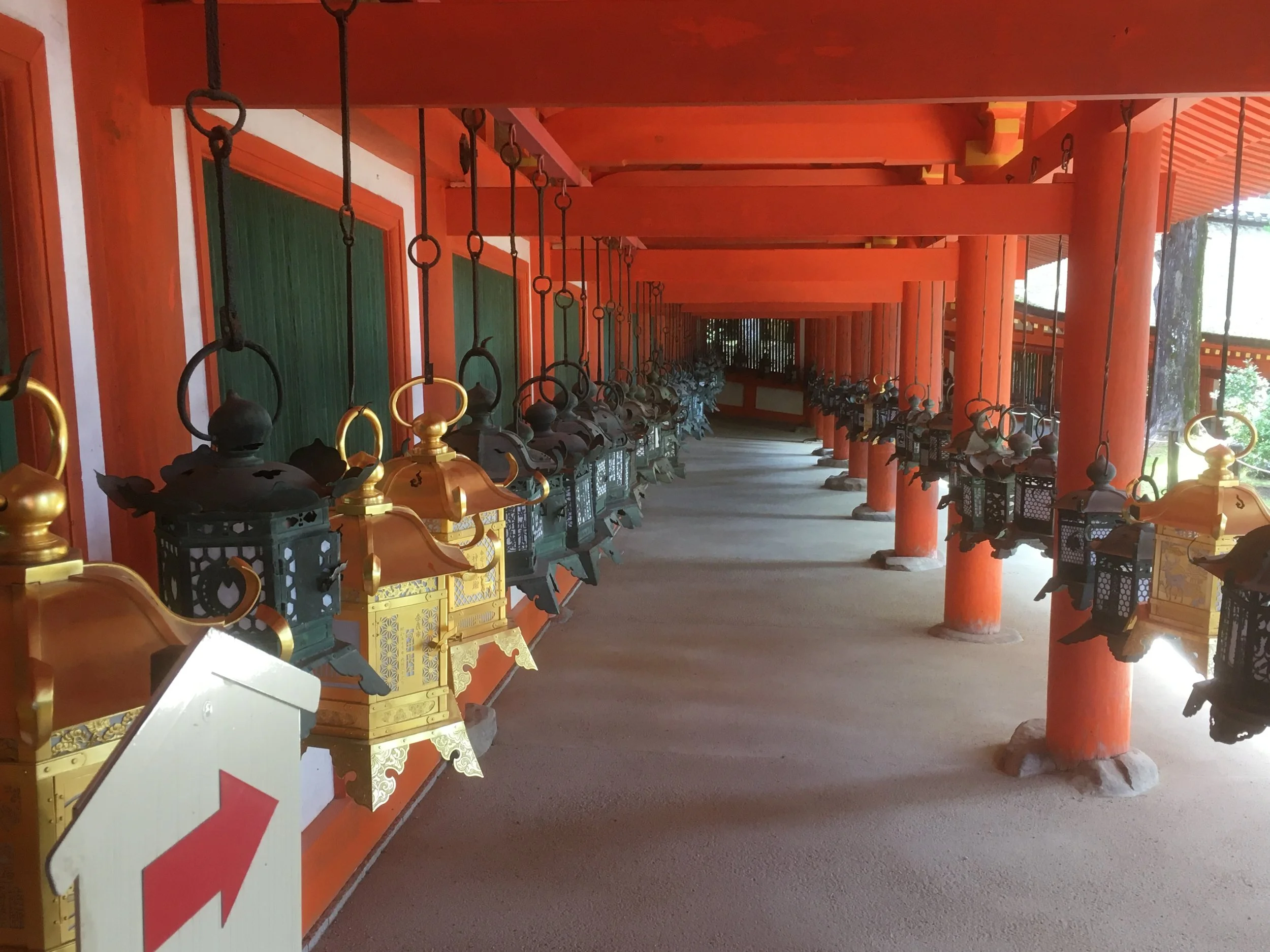 Row of decorative hanging lanterns along a corridor at a Japanese temple or shrine, with orange wooden beams and columns.