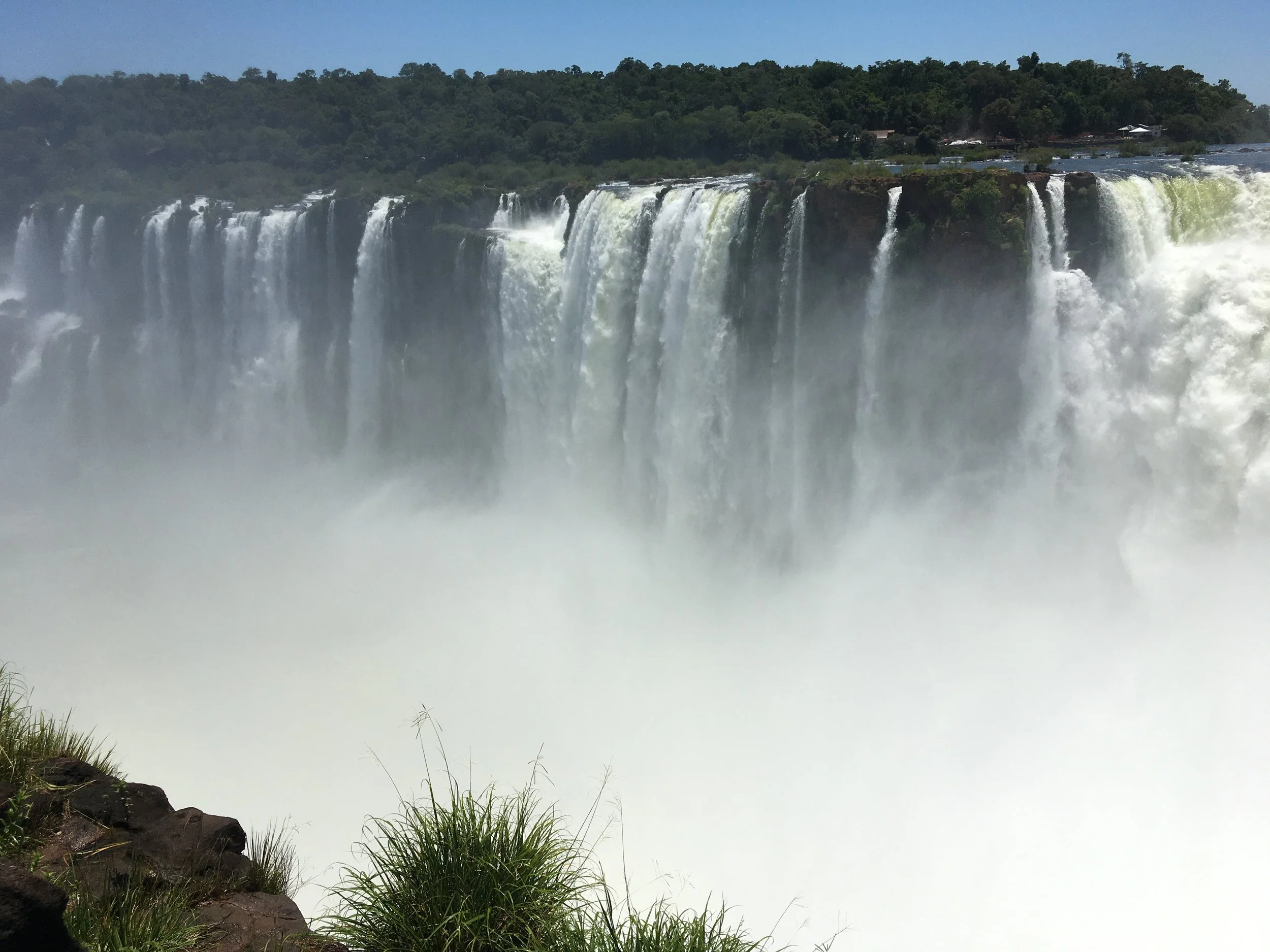 Niagara Falls with mist rising from the water and lush green trees in the background.