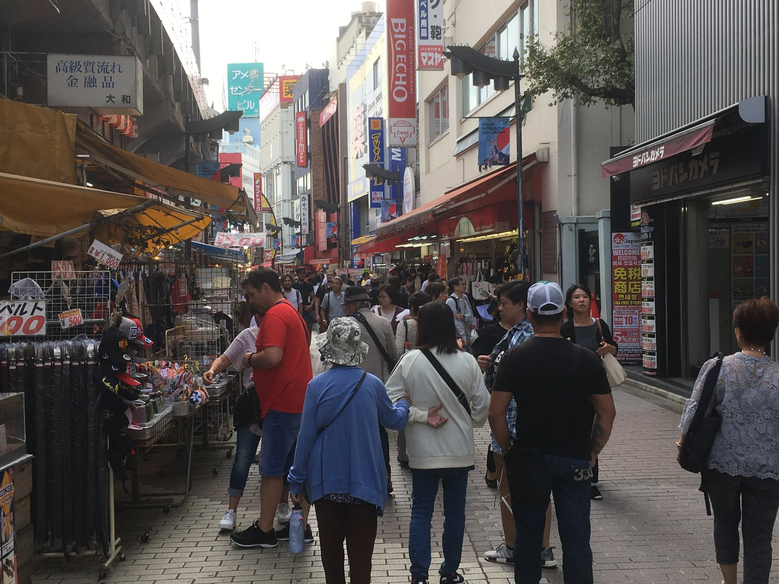 Crowded street market in Japan with various shops, signs, and pedestrians shopping and walking.