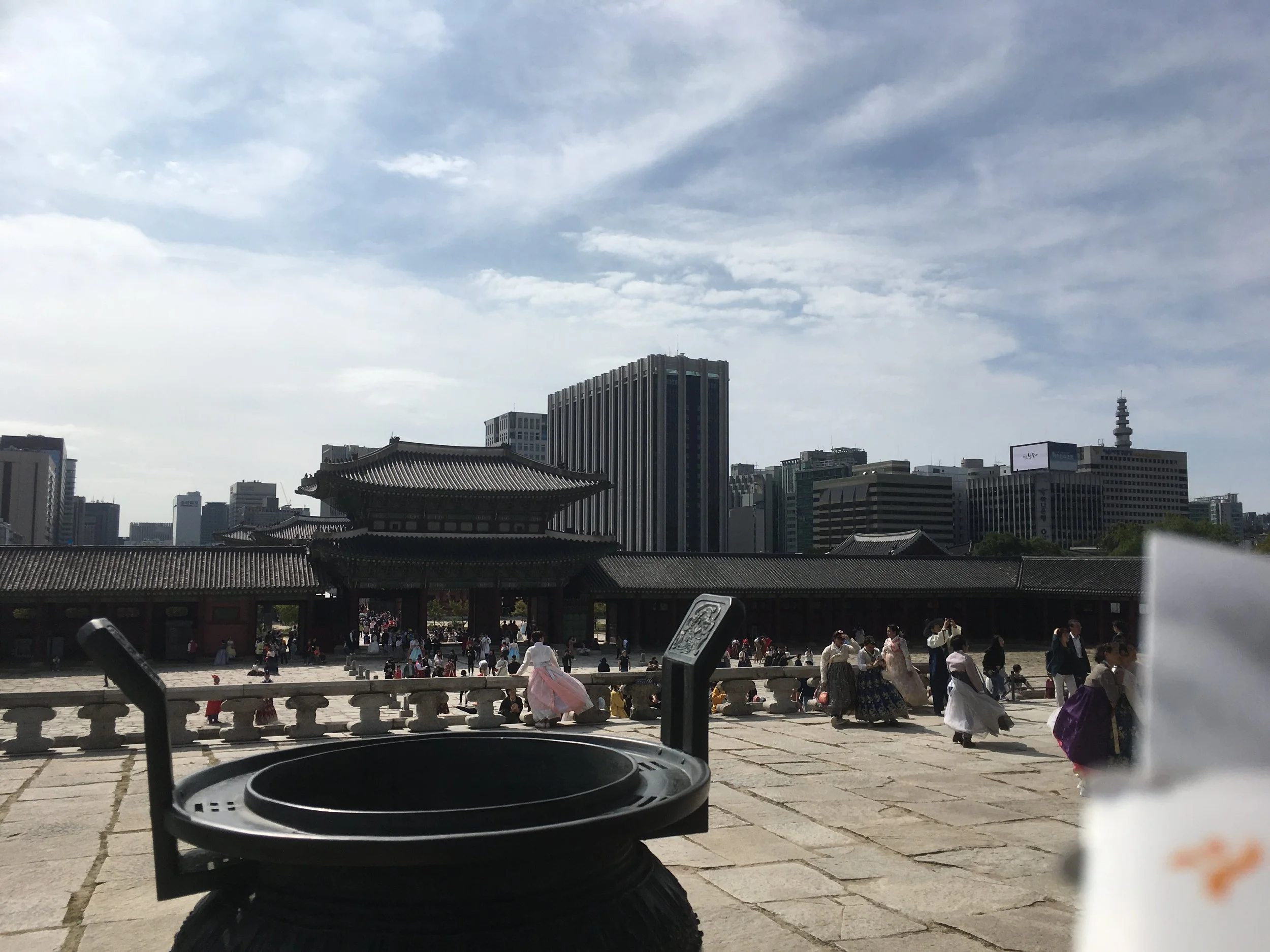 People dressed in traditional clothing at Gyeongbokgung Palace in Seoul, South Korea, with modern skyscrapers in the background.