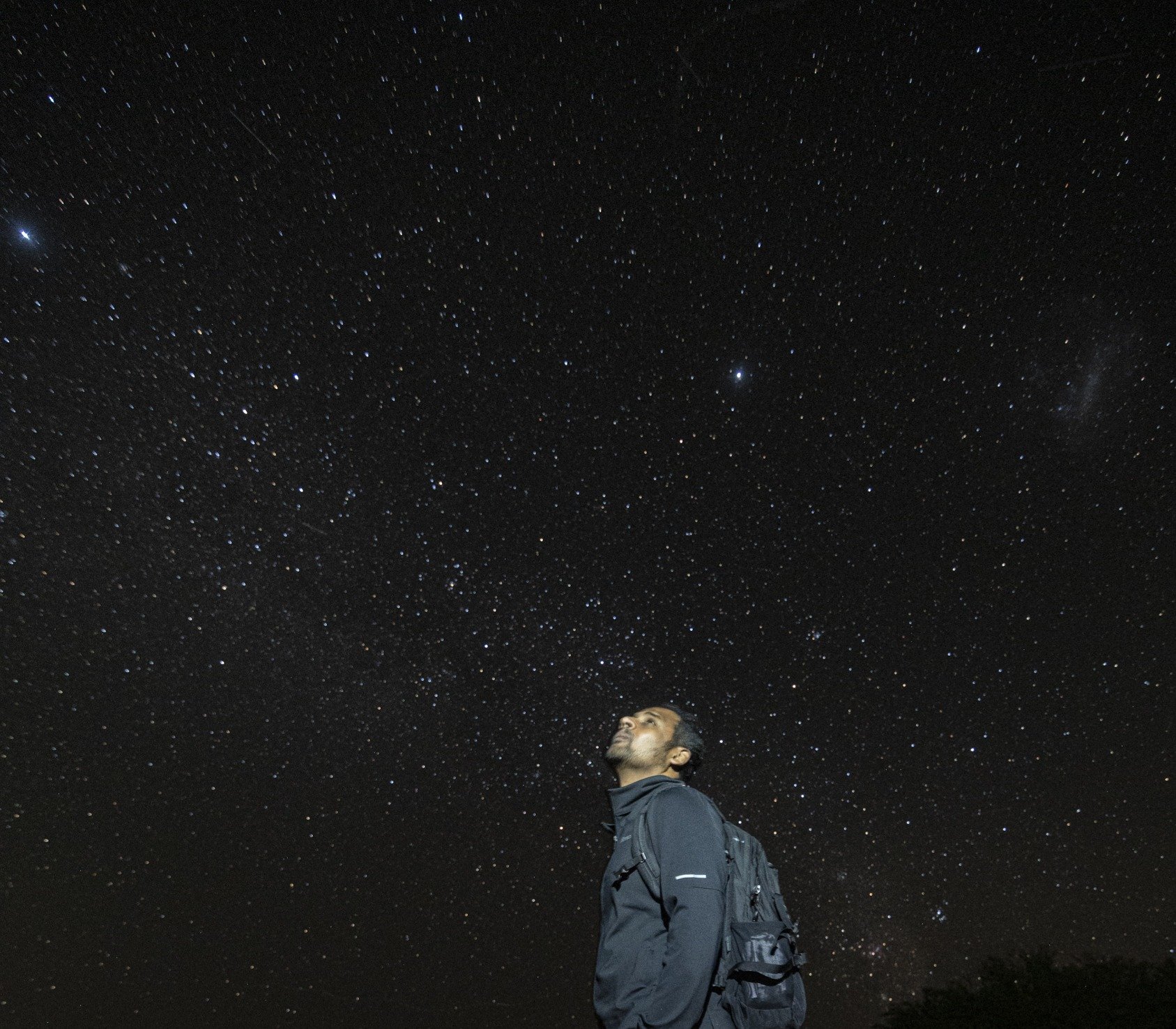A person with a backpack looking up at a starry night sky.