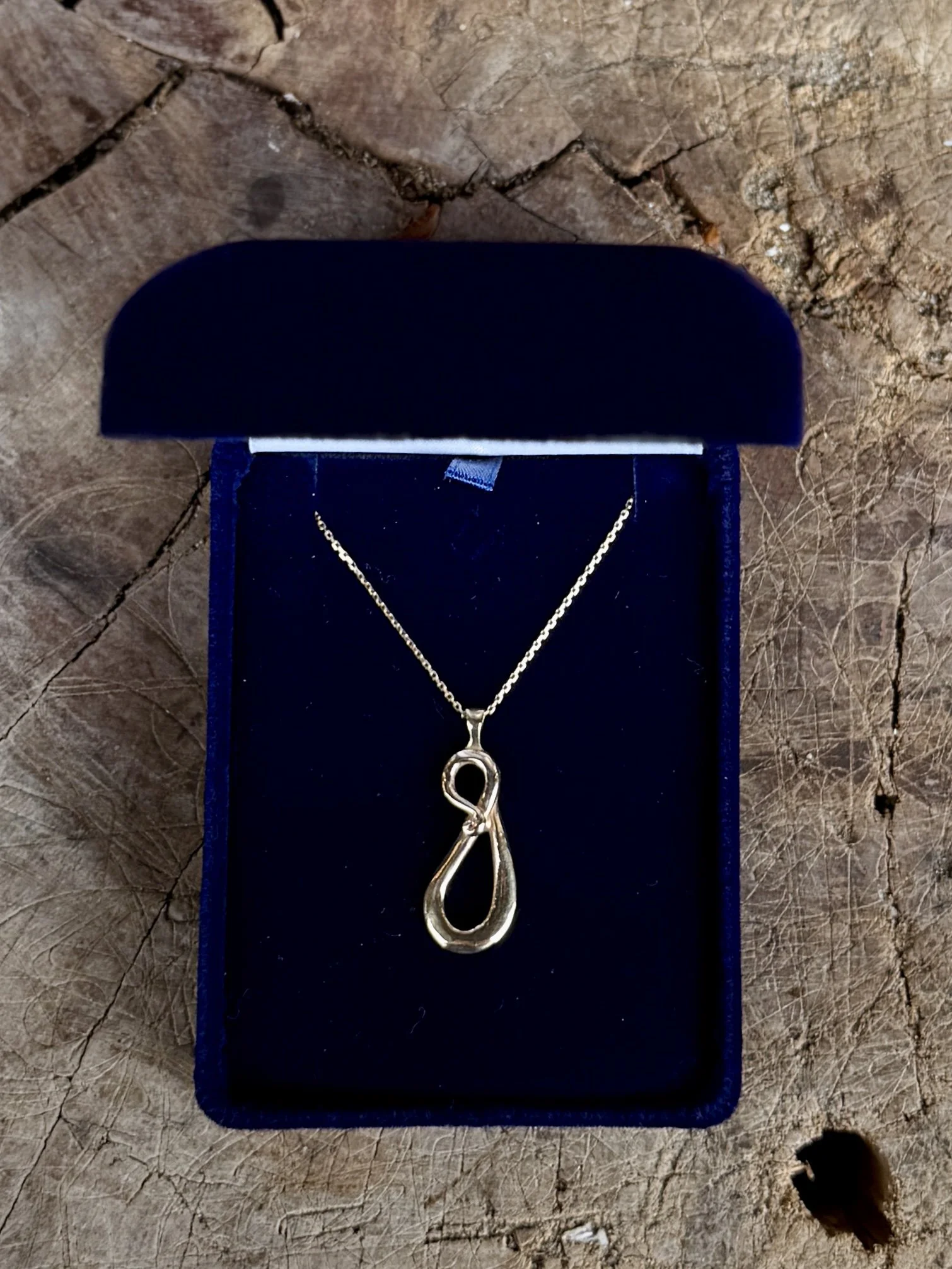 A silver necklace with a pendant shaped like a stylized question mark, displayed inside a navy-blue jewelry box with a soft interior.