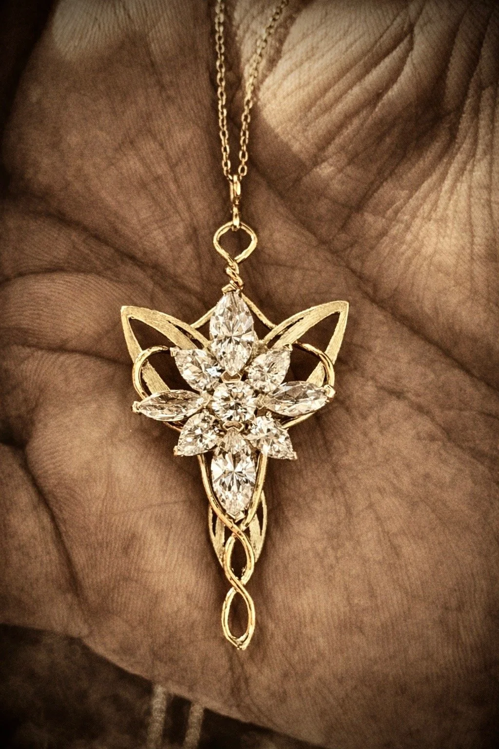Gold necklace with a large, ornate butterfly-shaped pendant featuring multiple clear gemstones, held against a person's hand.