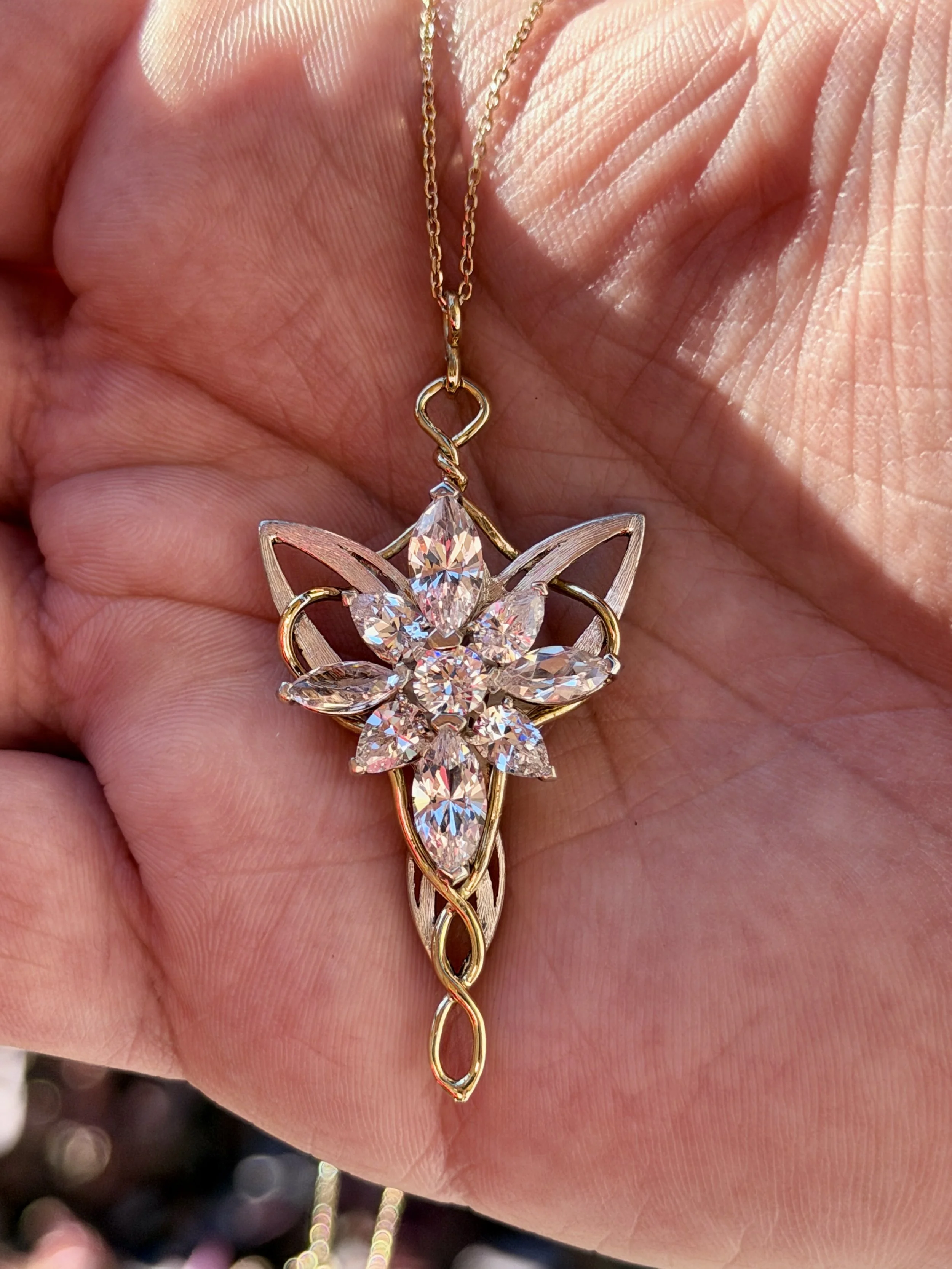 A gold necklace with a butterfly-shaped pendant adorned with clear, sparkling gemstones, held in a person's hand.