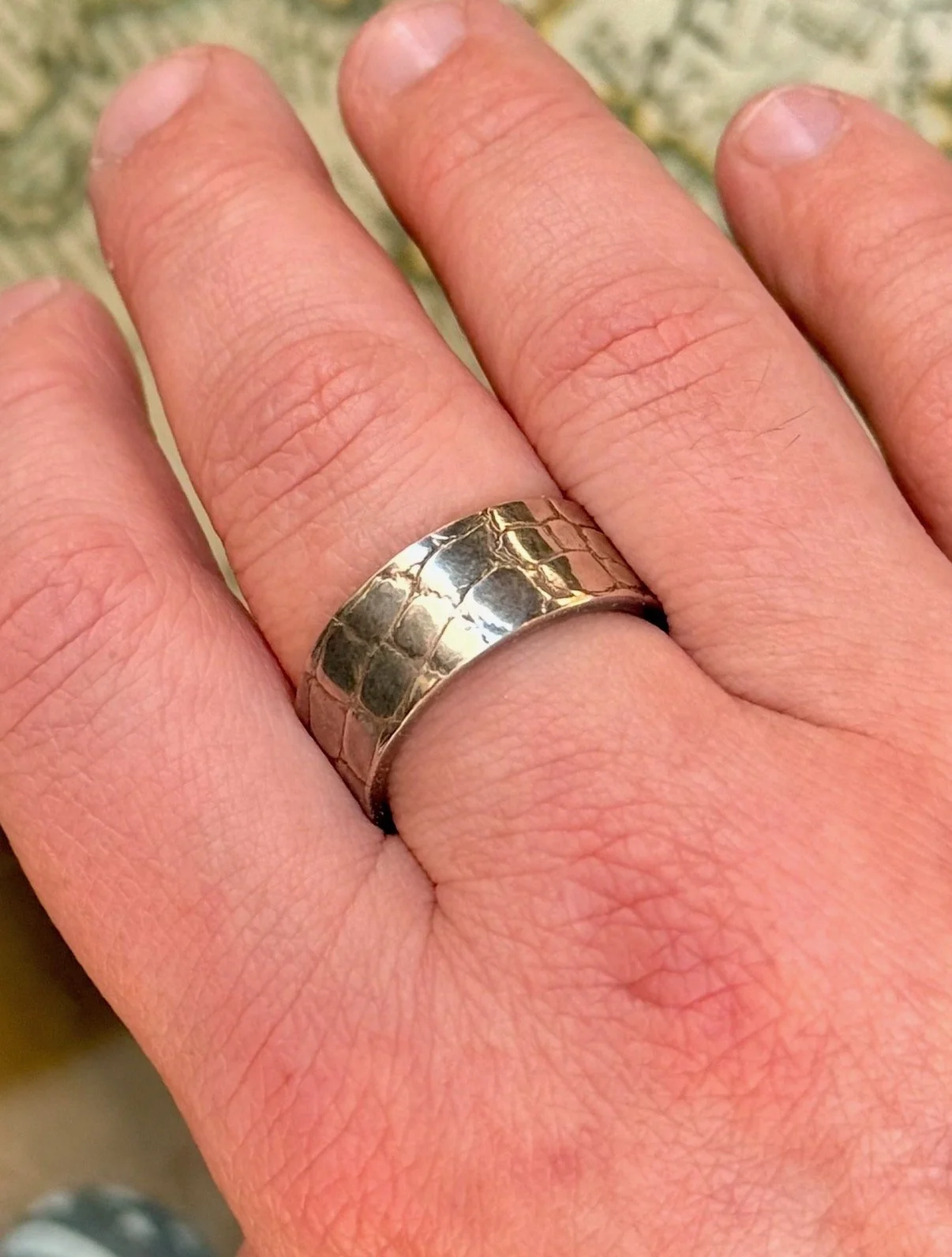 Close-up of a hand wearing a wide silver ring with a textured, patterned surface.