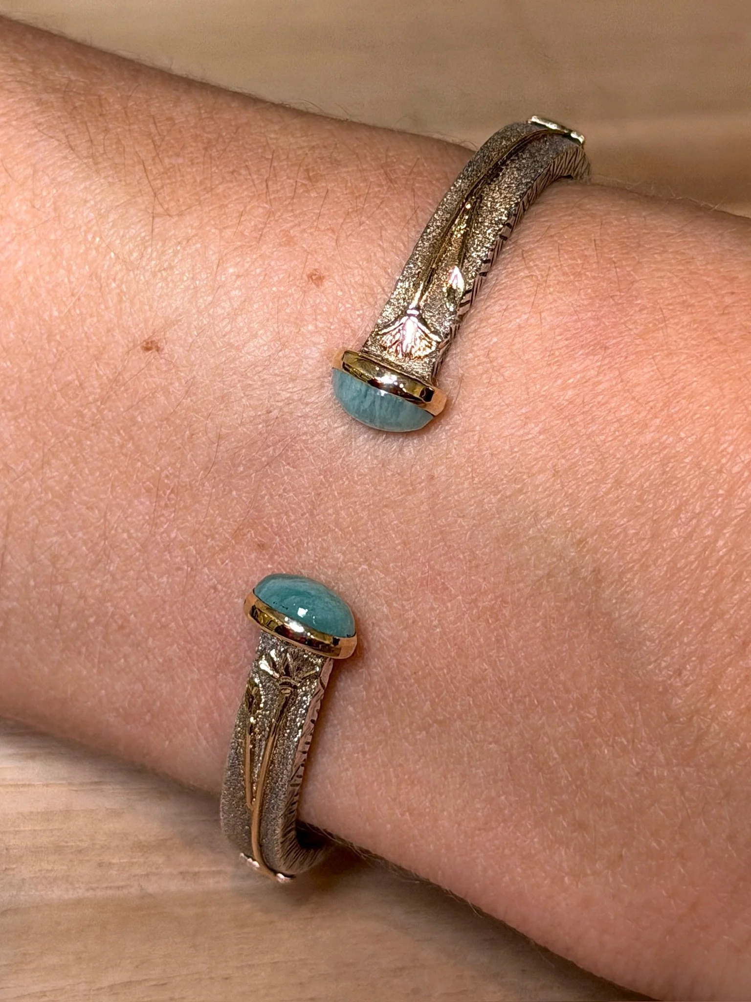 A person's wrist wearing two silver bangles with oval turquoise stones and intricate designs on the sides.