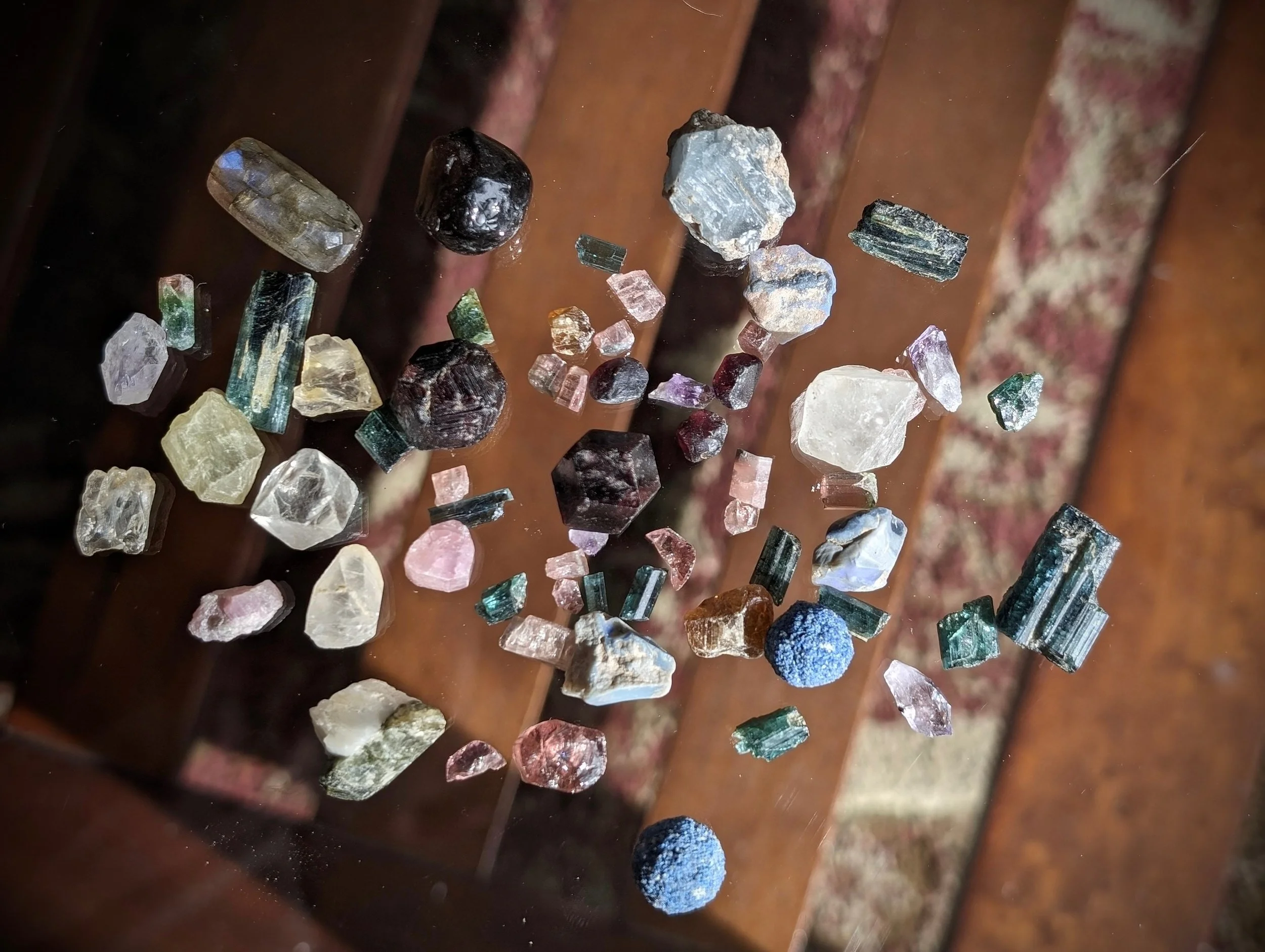 Various small, colorful gemstones and mineral crystals scattered on a reflective surface.