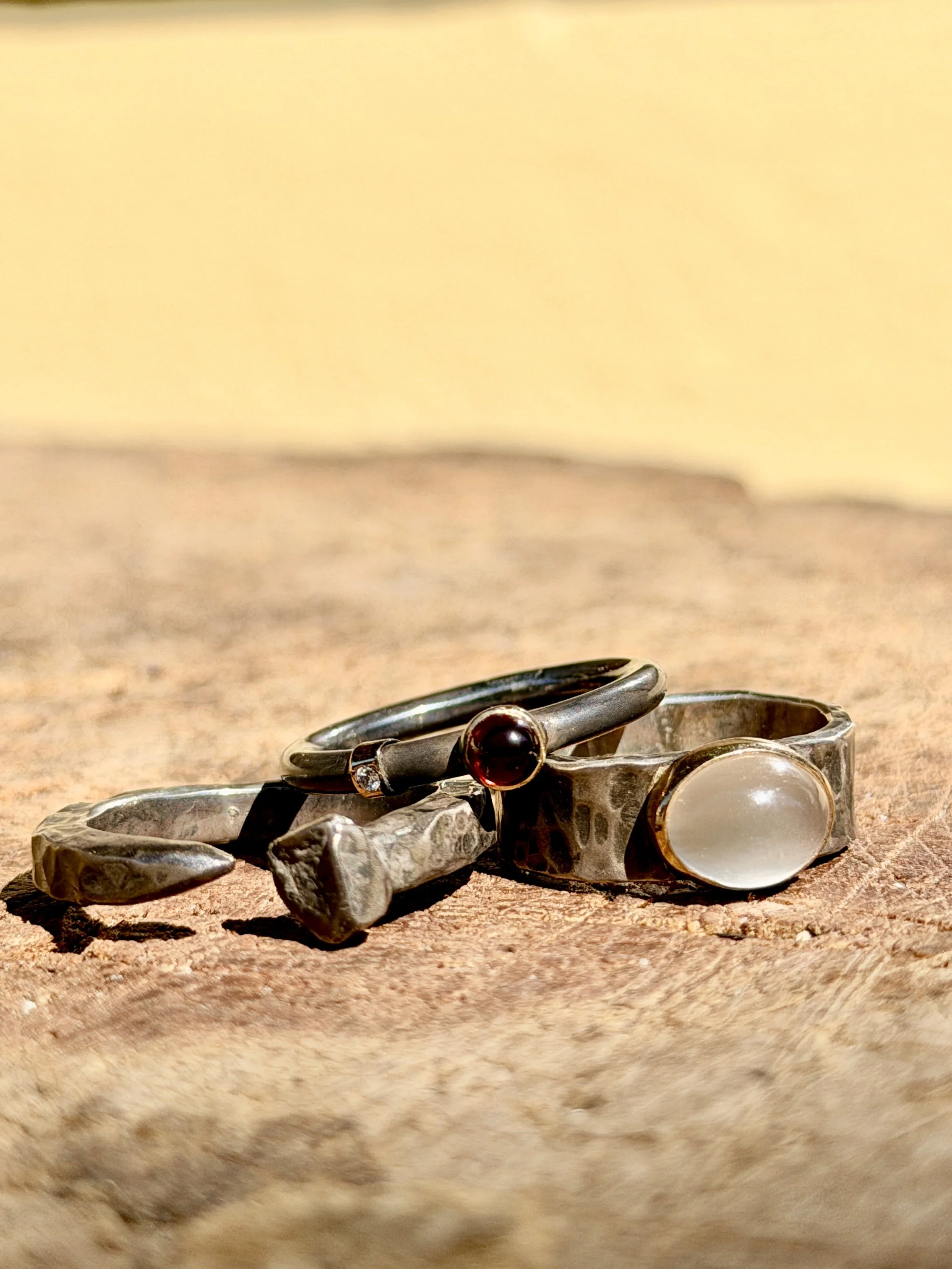Three silver rings with distinctive designs on a wooden surface against a yellow background.