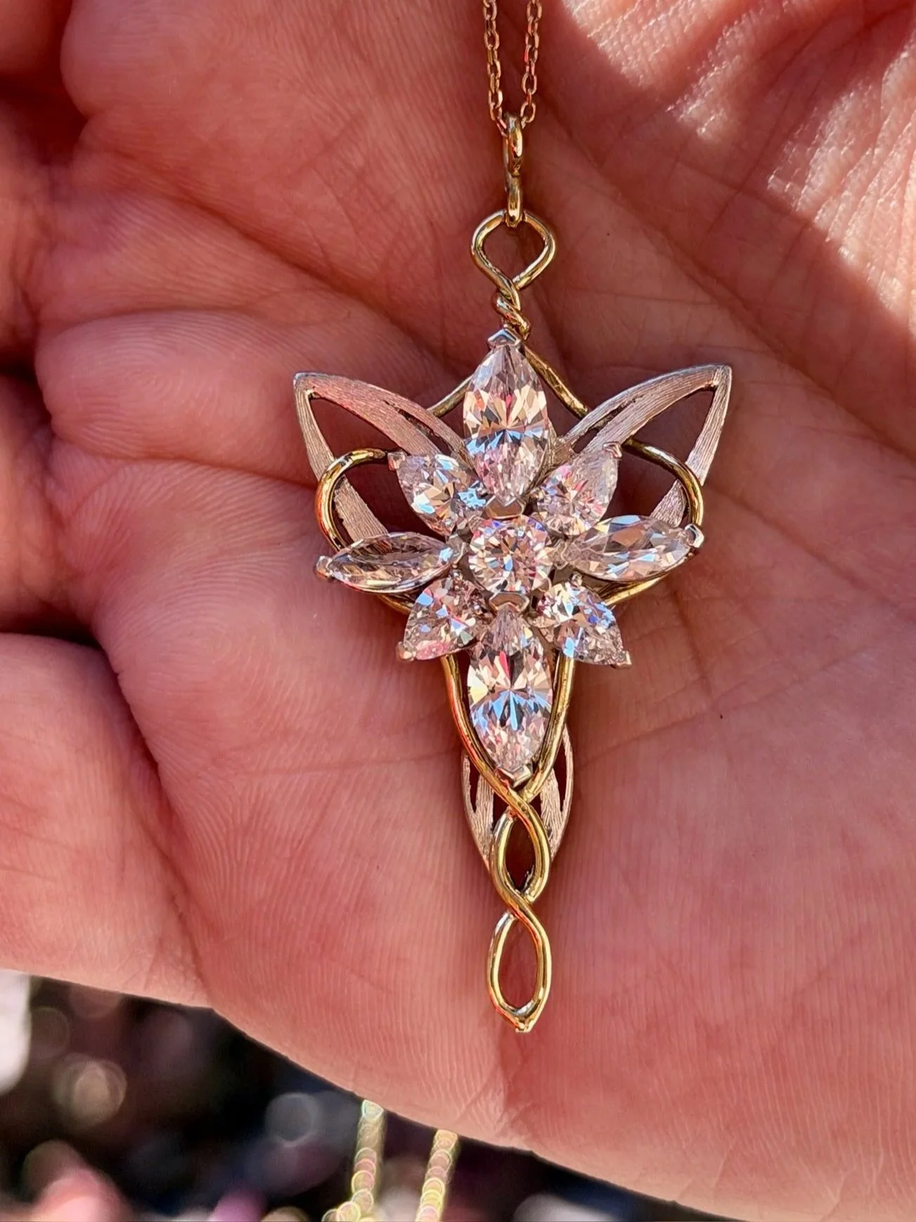 A pendant necklace featuring a gold chain and an intricate gold and silver floral design with large clear gemstones, held in a person's hand.