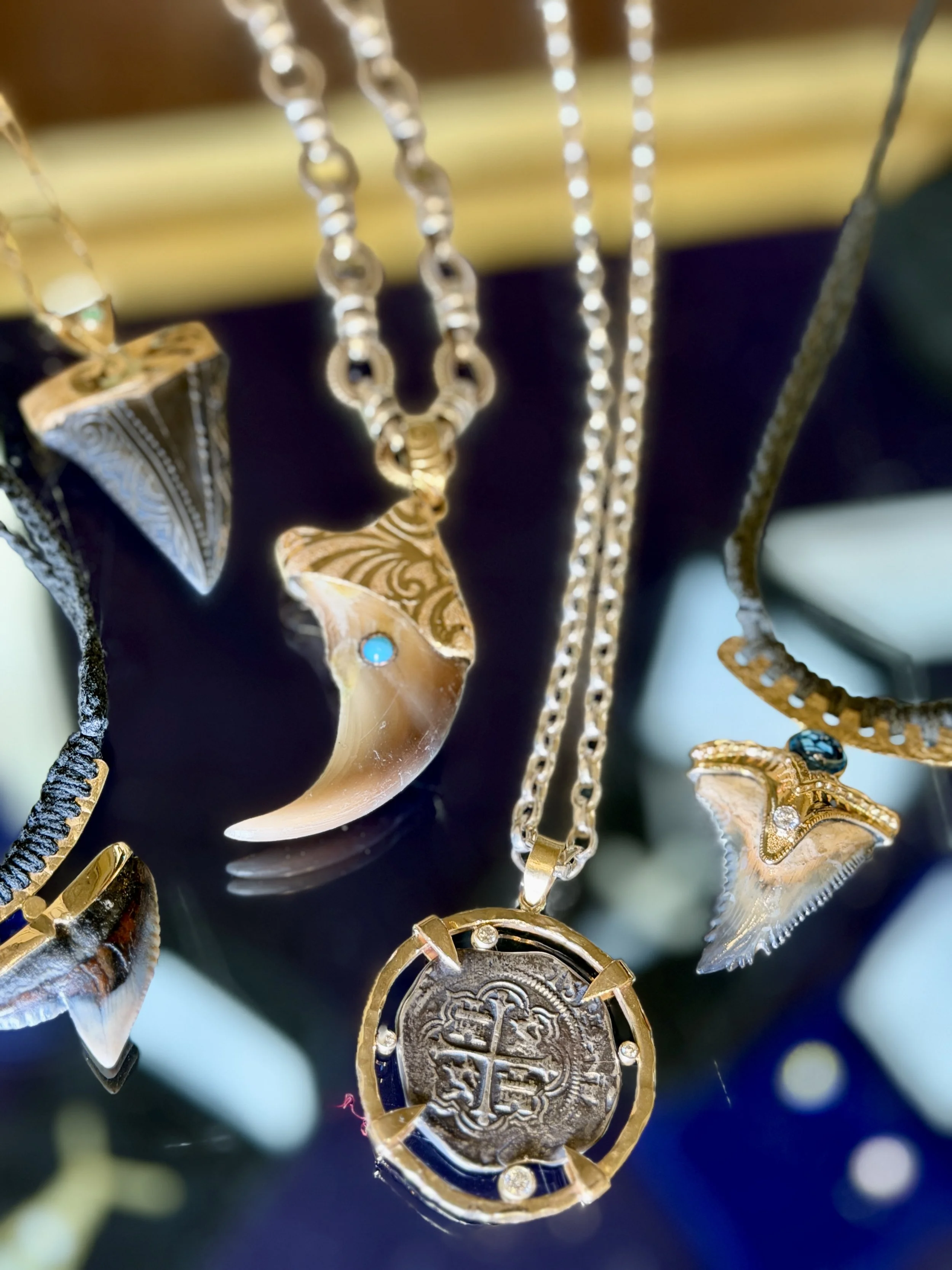 Close-up of gold jewelry including necklaces, pendants, and earrings, with shell and gemstone designs, displayed against a dark background.