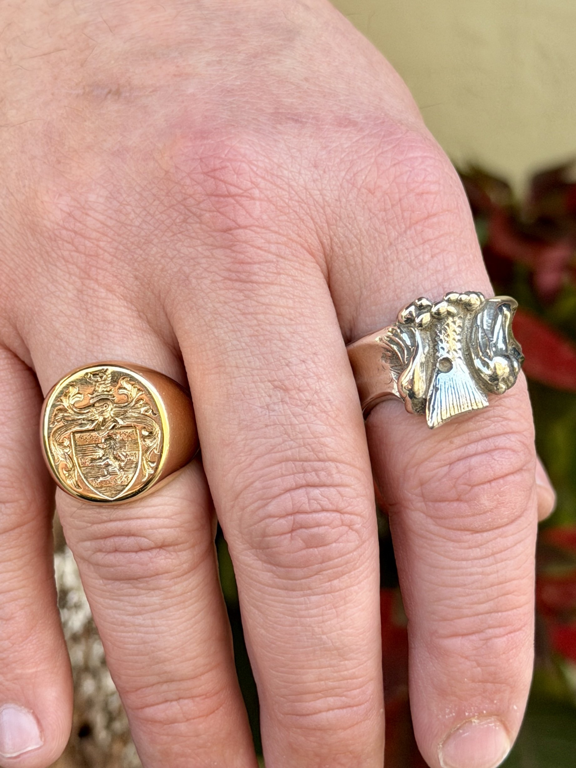 Close-up of a hand wearing two rings, one gold with a crest and the other silver with raised design.
