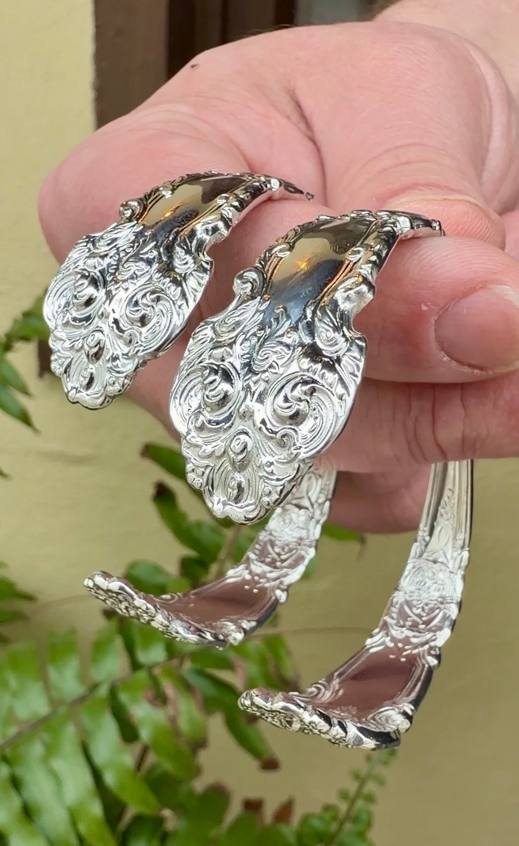 A person is holding a silver bracelet and a pair of matching earrings with ornate, swirling designs, featuring reflective surfaces and detailed craftsmanship.