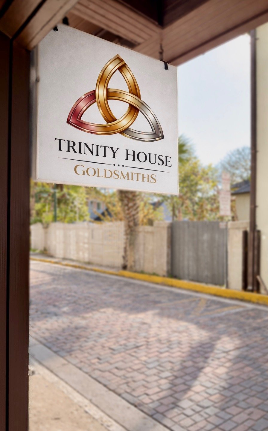 Sign for Trinity House Goldsmiths hanging outside, showing a three intertwined rings in gold, silver, and rose gold above the text.