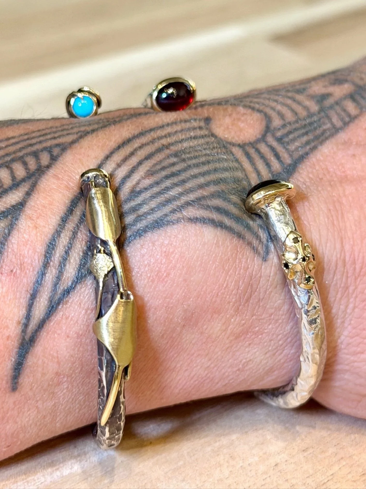 Close-up of a hand with a star tattoo, wearing several gold and silver rings with various gemstones.