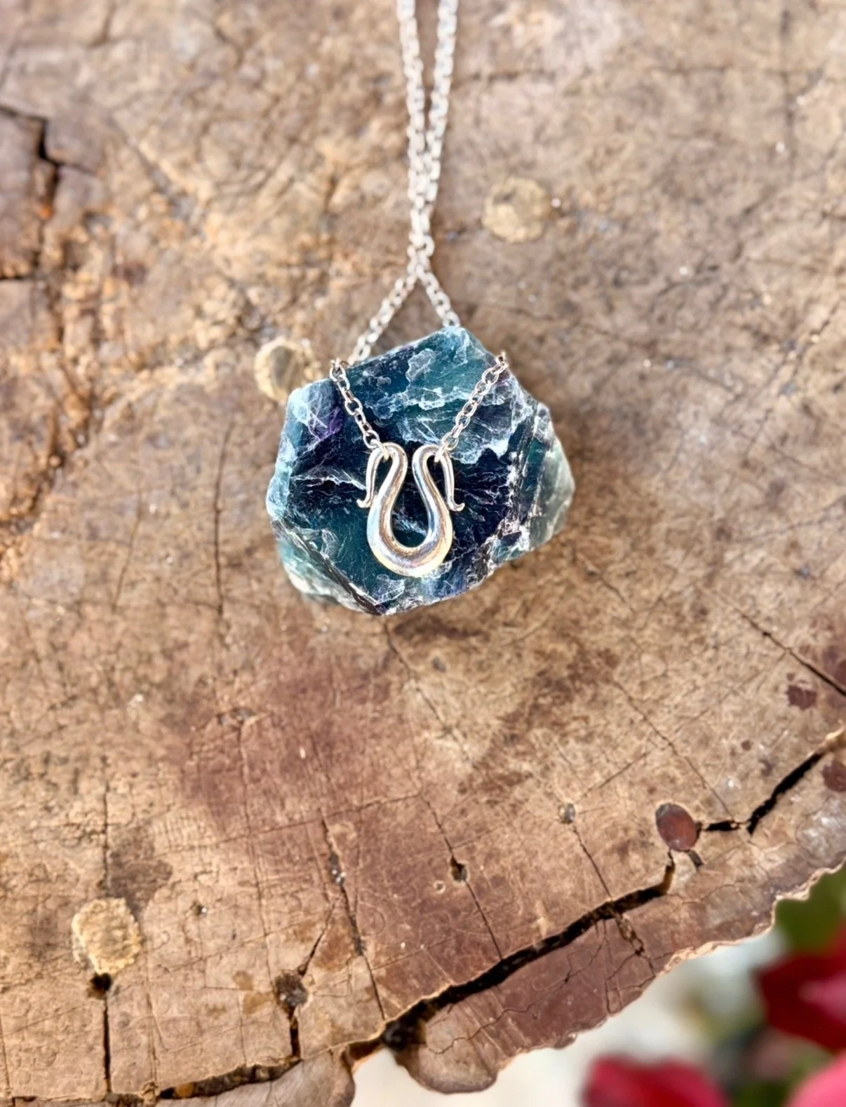 A silver necklace with a horseshoe pendant, hanging on a piece of rough, weathered wood.