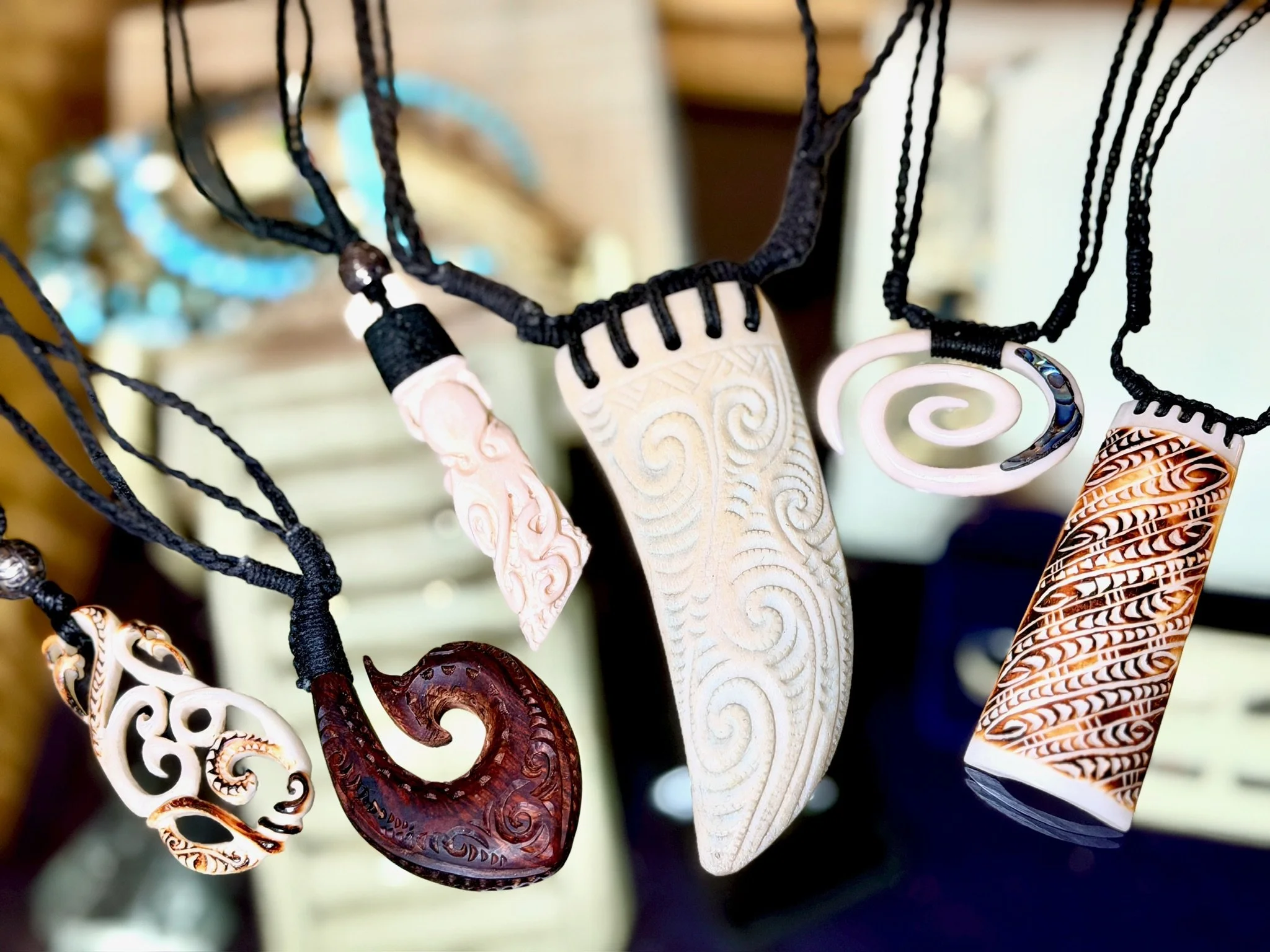 Collection of carved pendant necklaces made from bone, wood, and shell, hanging on black cords.