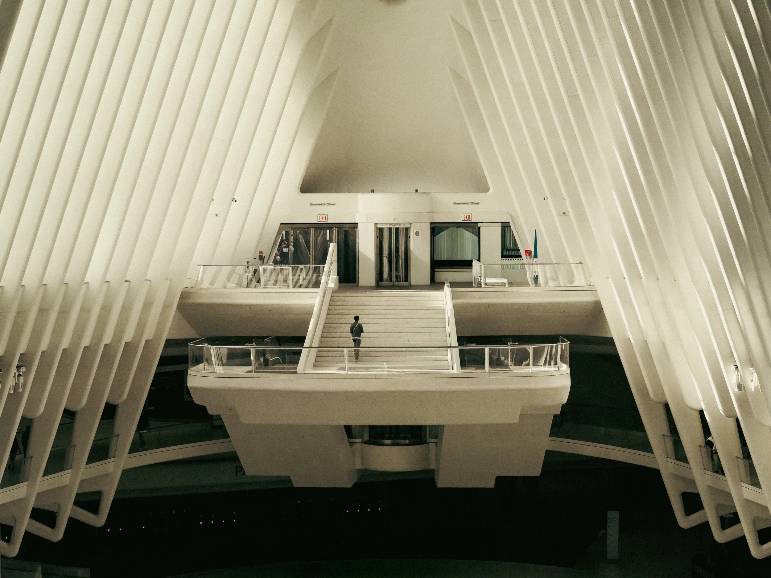 Interior view of a modern building with white structural ribs, stairs, and a person walking near the staircase.