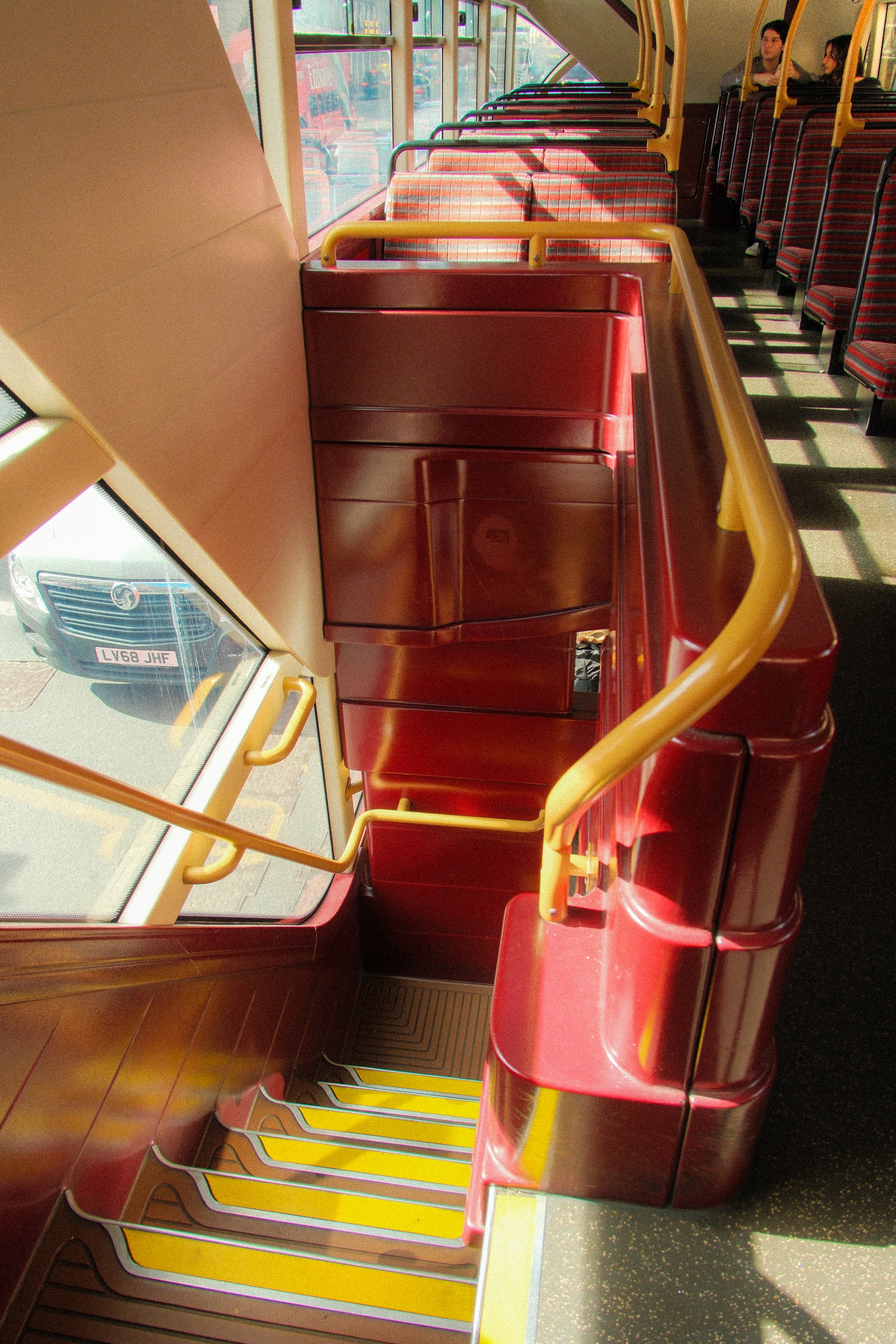 Interior of a bus showing yellow handrails and red seats with a few passengers. The photo is taken from the top of the stairs near the front door, looking towards the back of the bus.