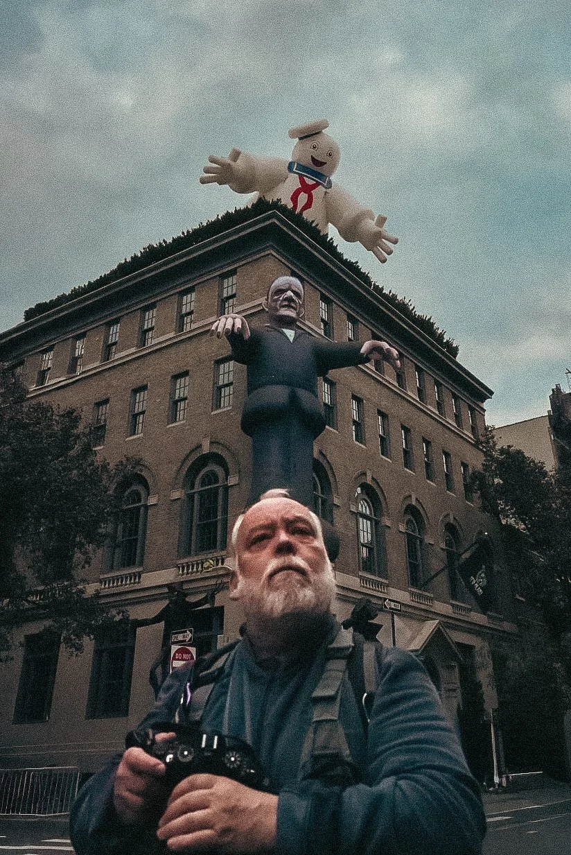A person with a backpack and camera stands in front of a building with a large statue of a man. An inflatable chef character is on the roof of the building.