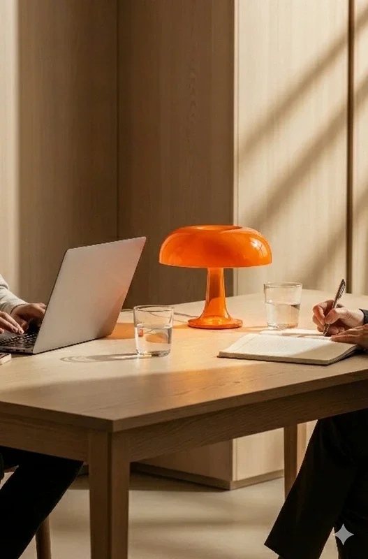 Two people sitting with a table between them. They have a computer and a notebook and they appear to be having a alignment meeting.