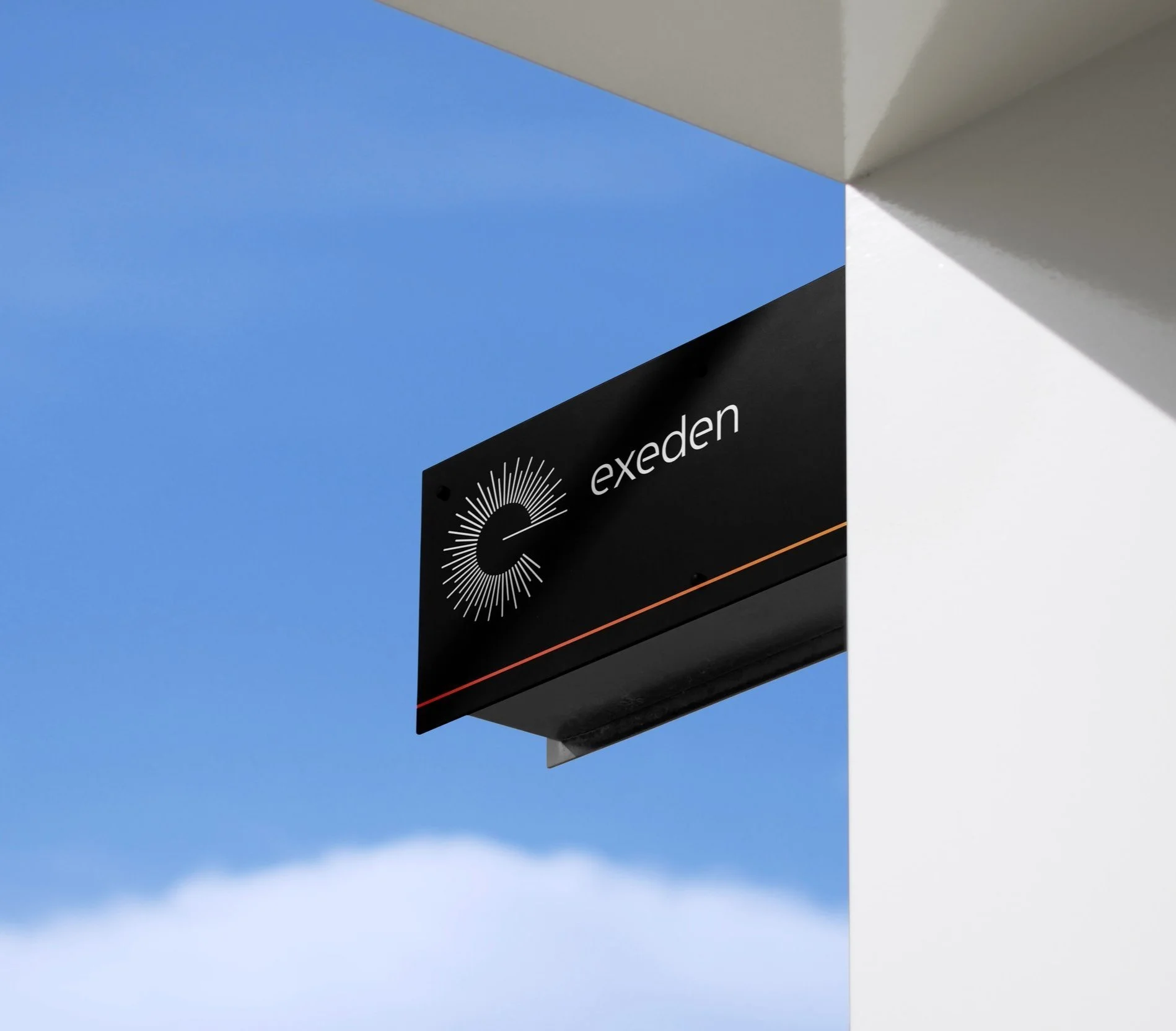 Black rectangular sign with the logo and name 'exeden' mounted on a white building under blue sky.