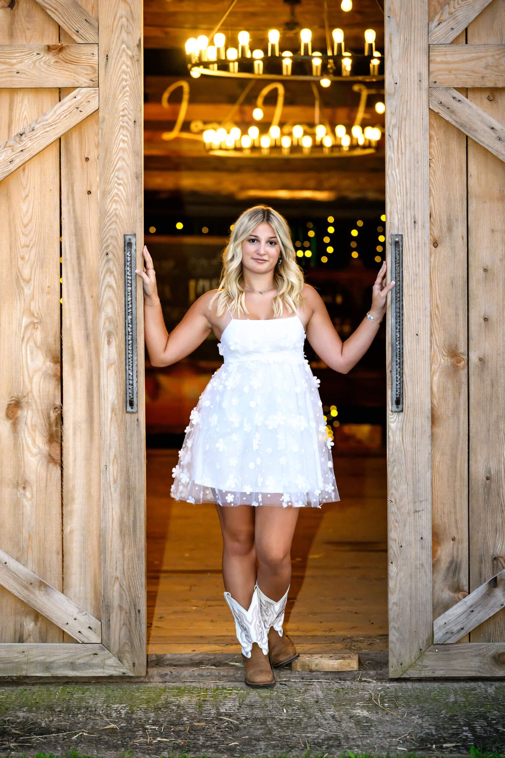Senior high school giri in white puffy dress and cowboy boots standing between barn doors portrait session